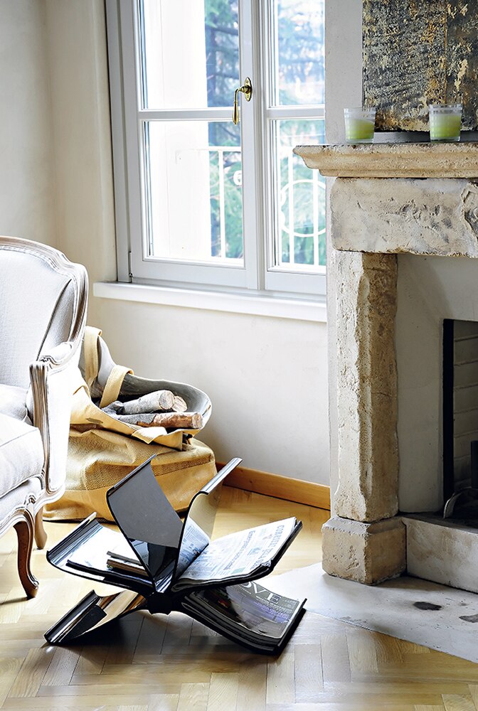 Schwarzer Kartell Zeitungsständer "Front Page" im Wohnzimmer neben Kamin und Sessel. Design Möbel für Zeitschriften.