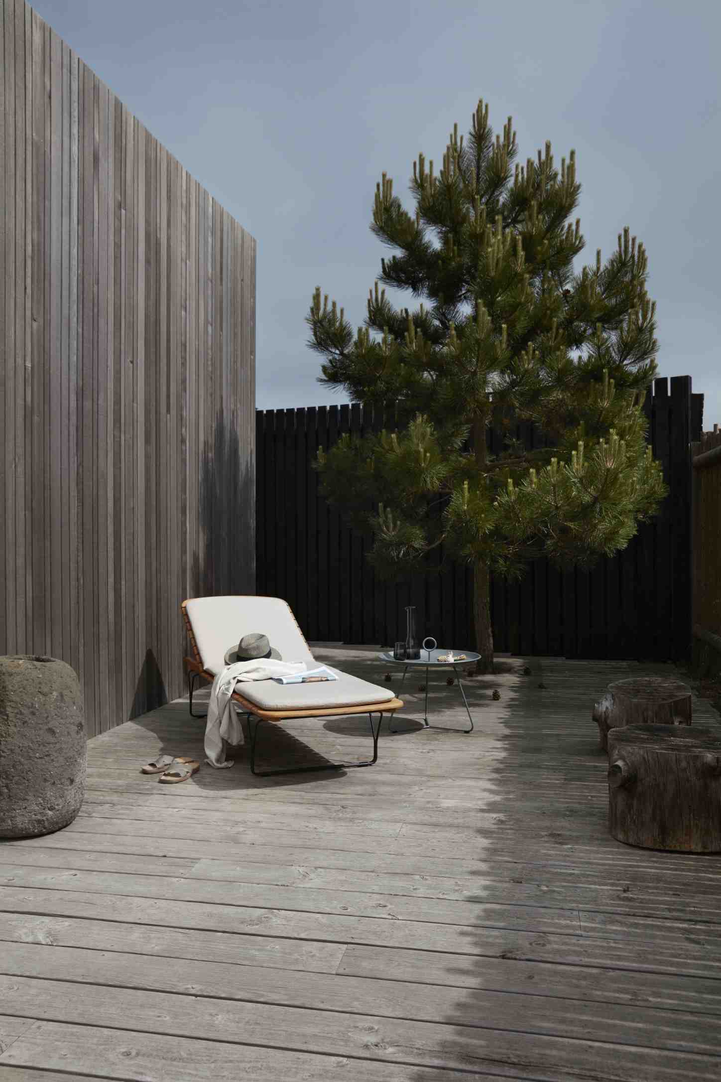 Houe Sonnenliege mit Molo Outdoor Kissen im Garten auf Holzterrasse, mit Hut und Buch.