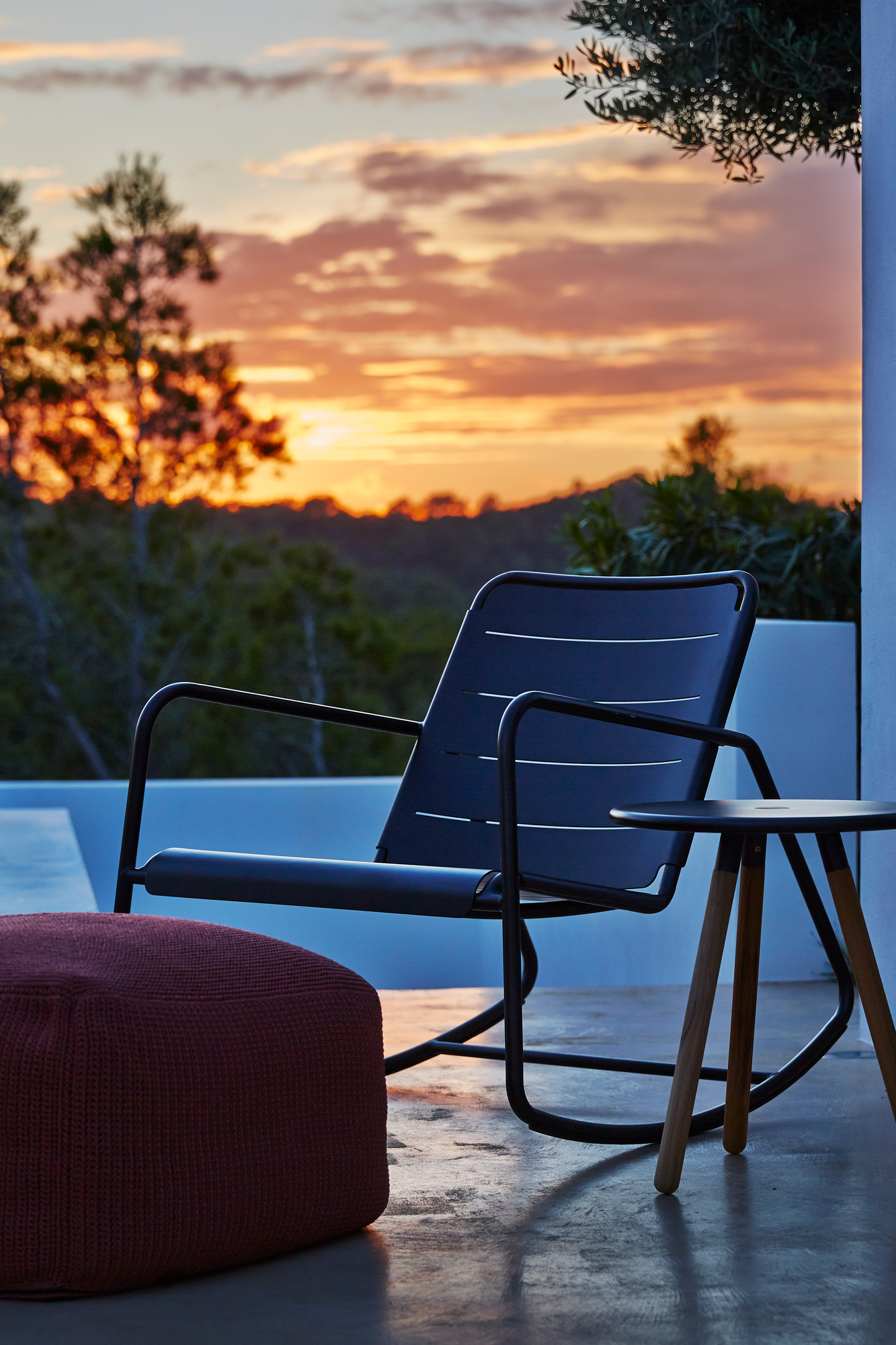 Cane-Line Schaukelstuhl für den Außenbereich, dunkelblau, mit Hocker und Beistelltisch bei Sonnenuntergang.