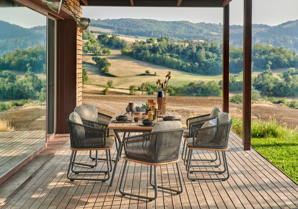 Denia Outdoor Esstisch von Weishäupl aus Teakholz mit Stühlen auf einer Terrasse.