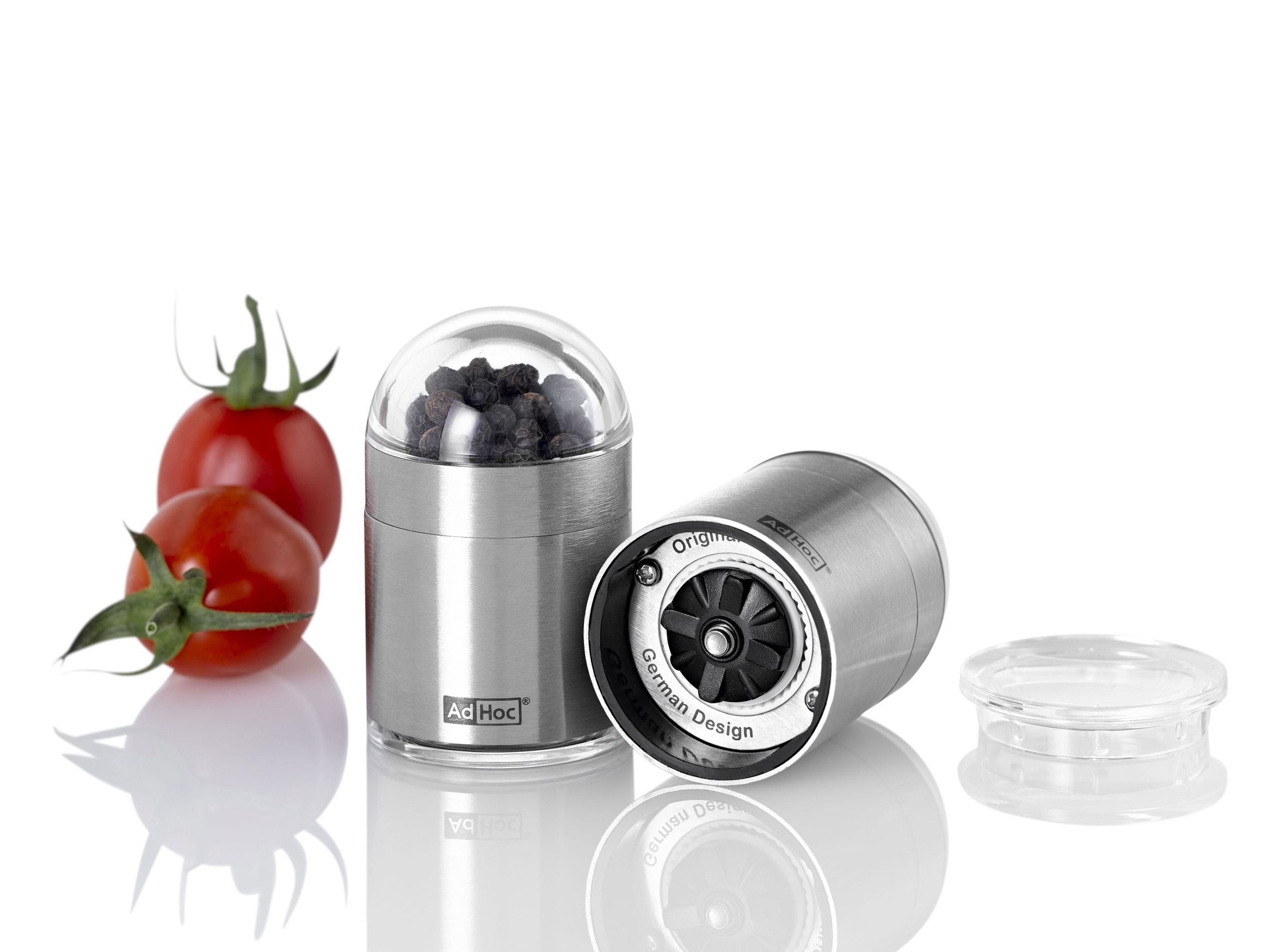 AdHoc Pfeffermühle und Salzmühle ToGo Set aus Edelstahl mit Tomaten im Hintergrund.