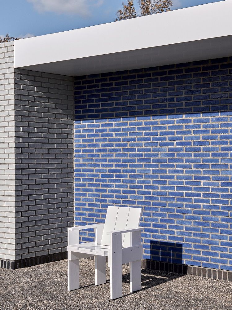 Weißer Crate Dining Chair Outdoor Stuhl von Hay vor blauer Backsteinmauer, moderne Gartenmöbel.