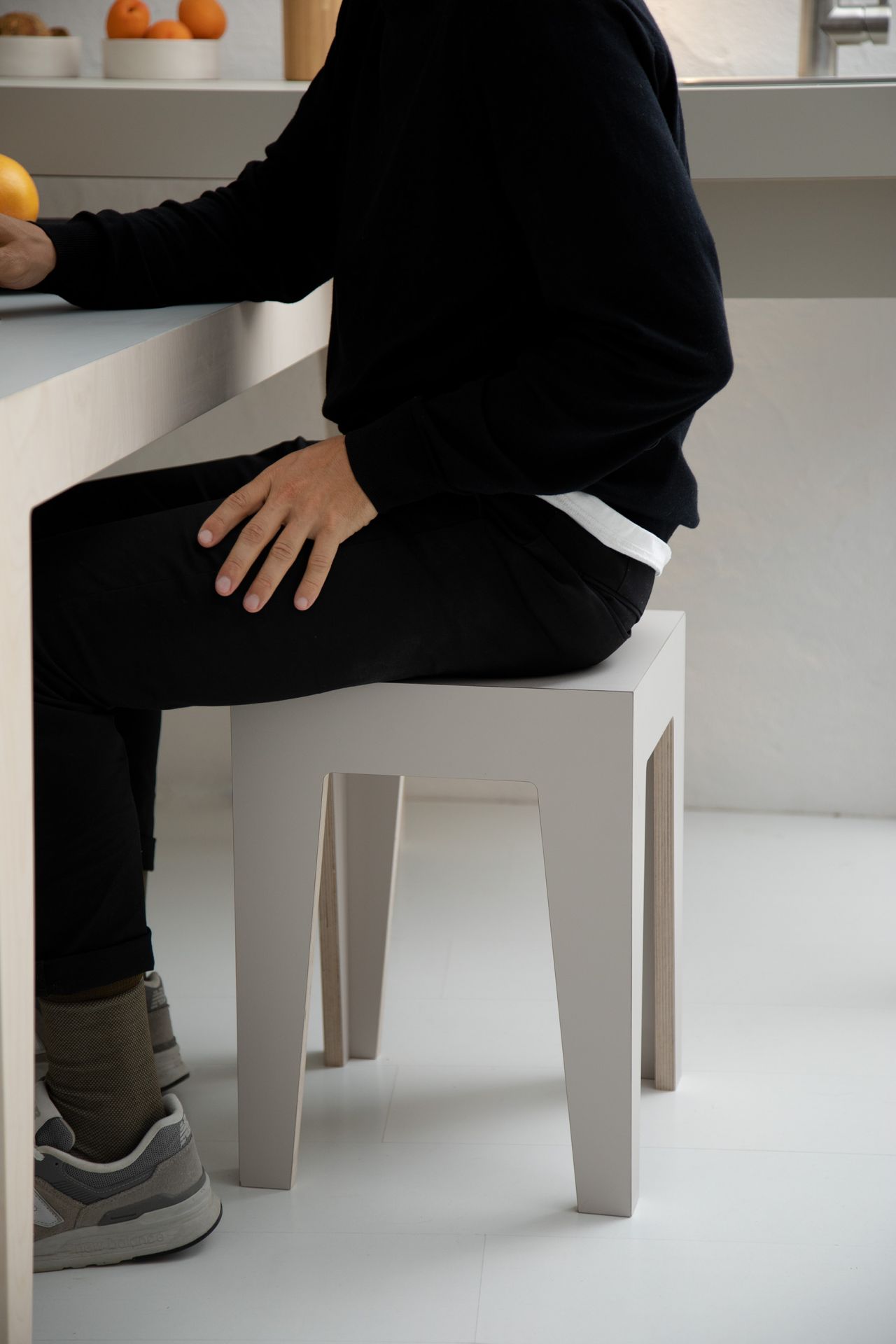 Mann sitzt auf modernem, grauem Hocker aus Holz. Minimalistisches Design für Esszimmer oder Küche.