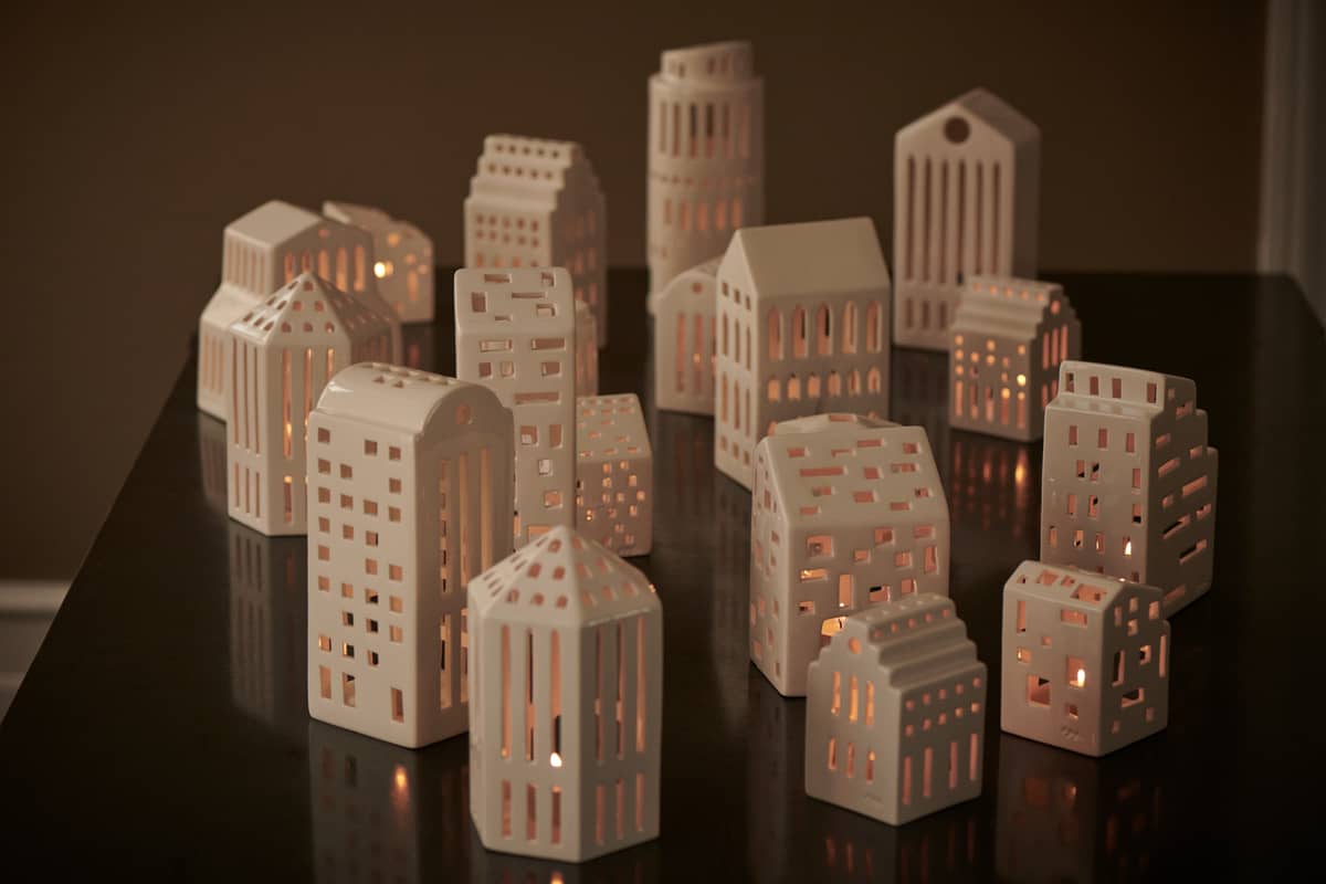 Nahaufnahme von mehreren weißen Kähler Urbania Lichthäusern, die auf einer dunklen Oberfläche stehen und warmes Kerzenlicht ausstrahlen.