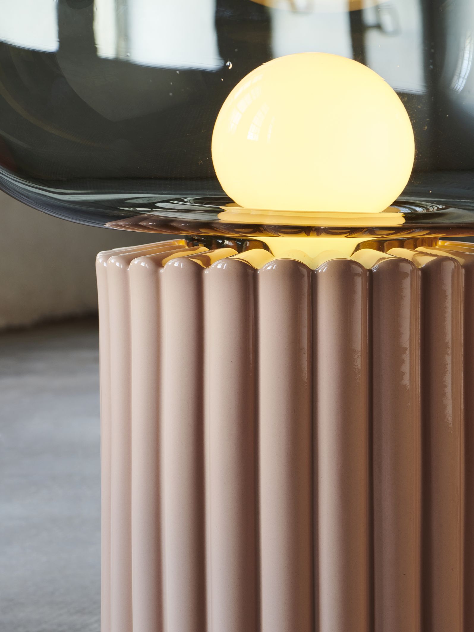 Detailaufnahme der Fungi Bodenleuchte in Warmbeige mit geriffeltem Sockel und leuchtender Kugel.