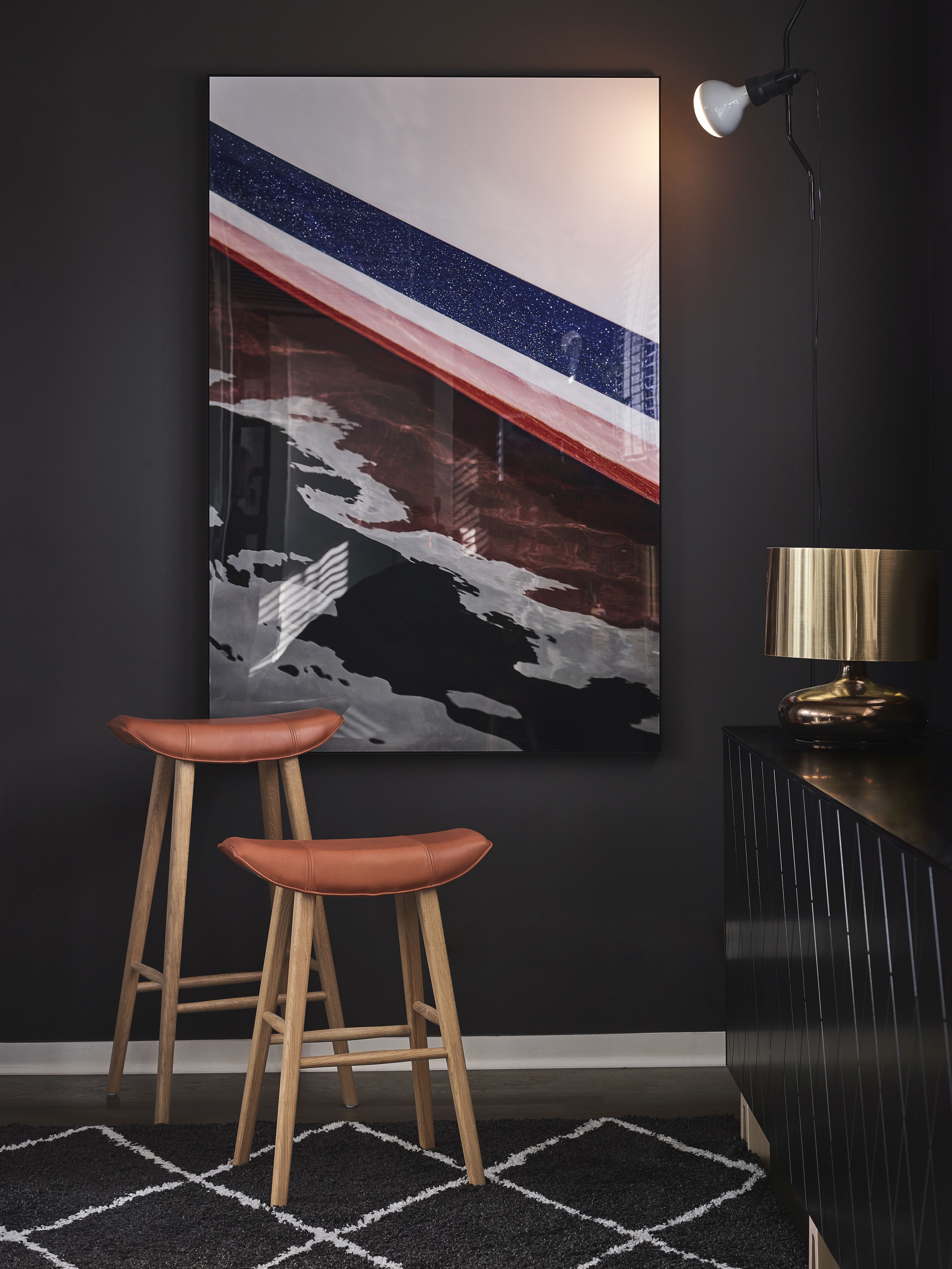 Zwei Kya Küchenhocker von Freifrau Manufaktur mit braunen Ledersitzen und hellem Holzgestell vor dunkler Wand.