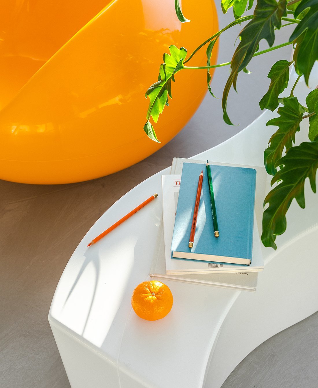 Detailaufnahme: Blauer Pastil Stuhl, Bücher, Stifte und Orange. Designklassiker für modernes Wohnen.