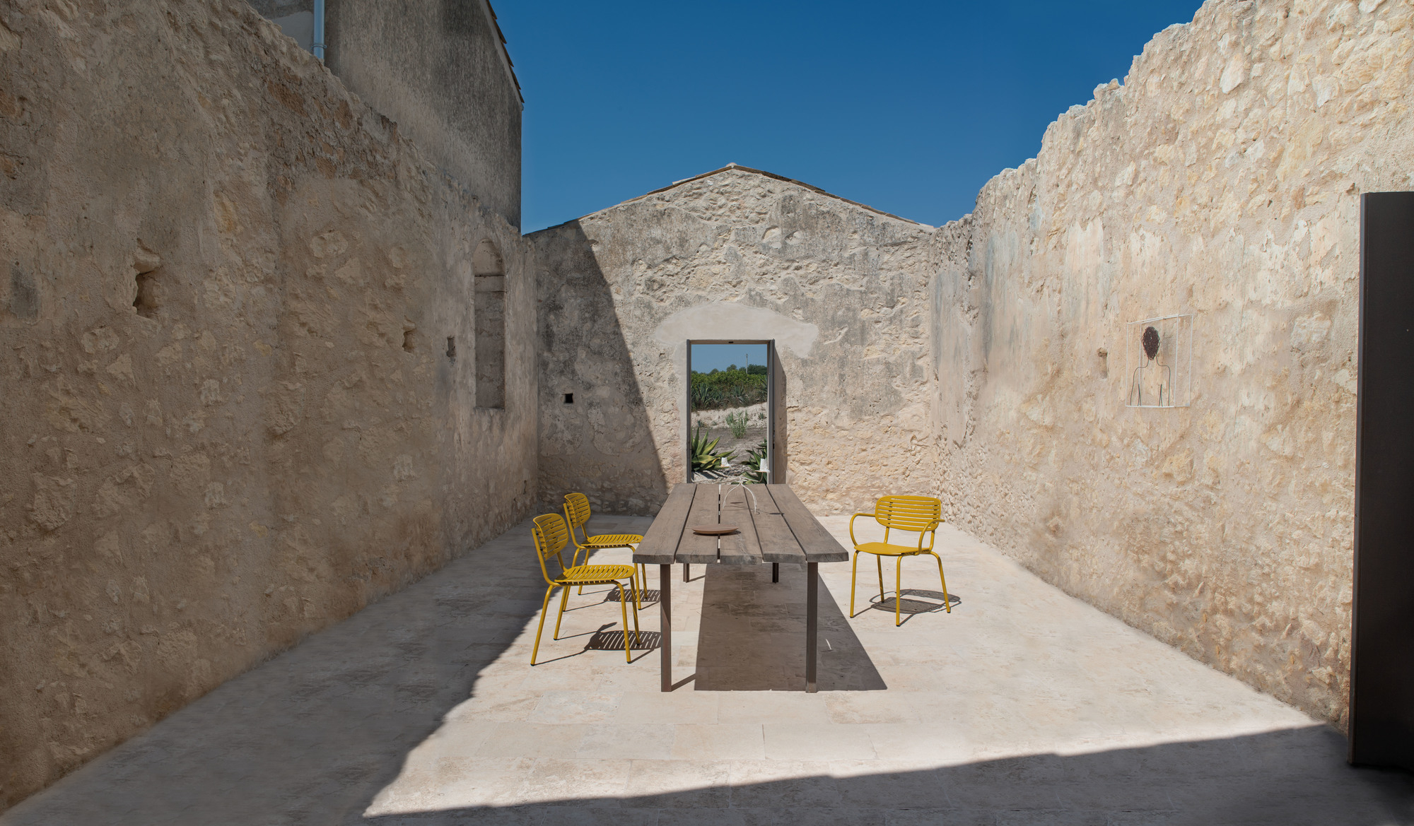 Gelbe Emu Stühle um einen Holztisch in einem mediterranen Innenhof. Outdoor Möbel.