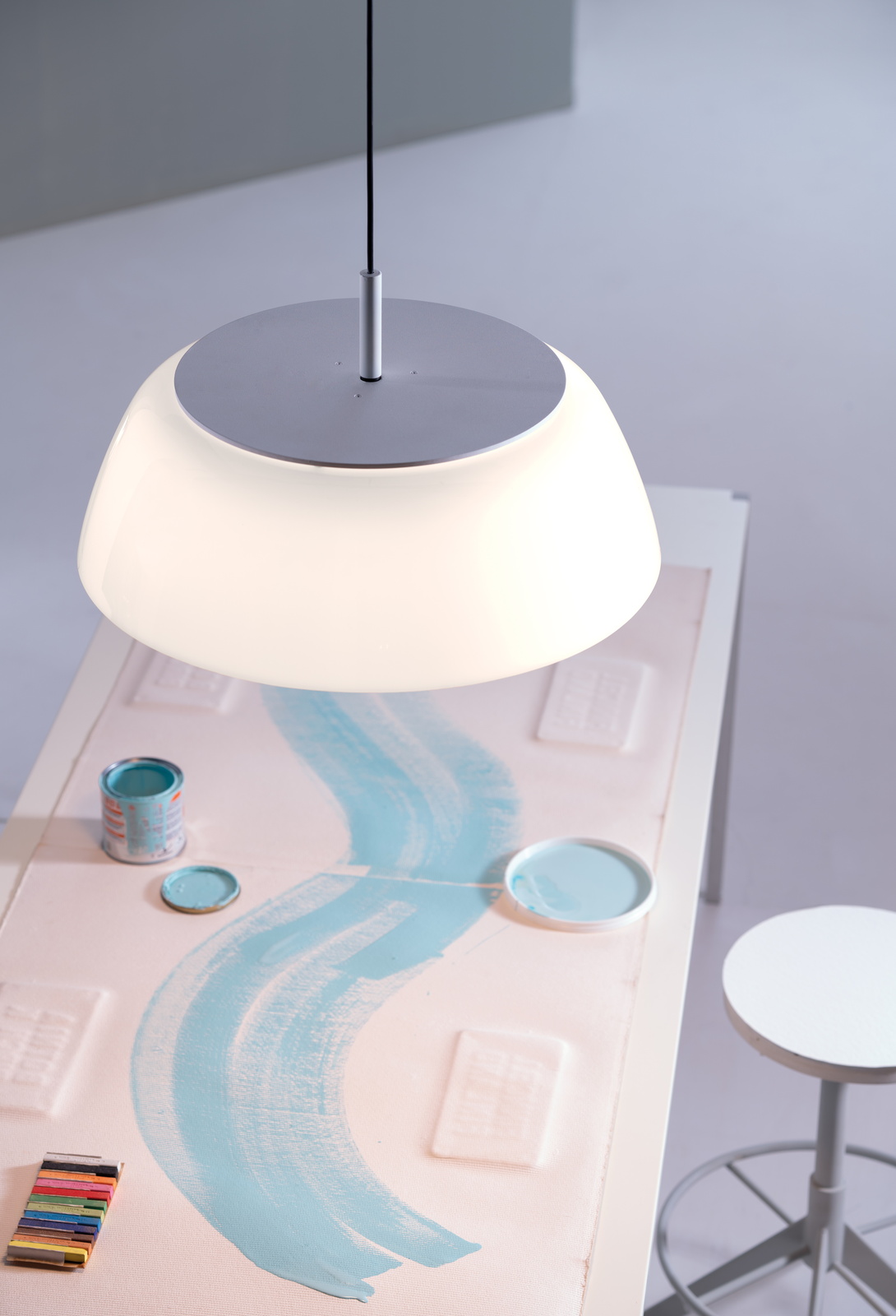 Onda Pendelleuchte von Martinelli Luce über einem Tisch mit Farbtöpfen und Pinselstrichen.