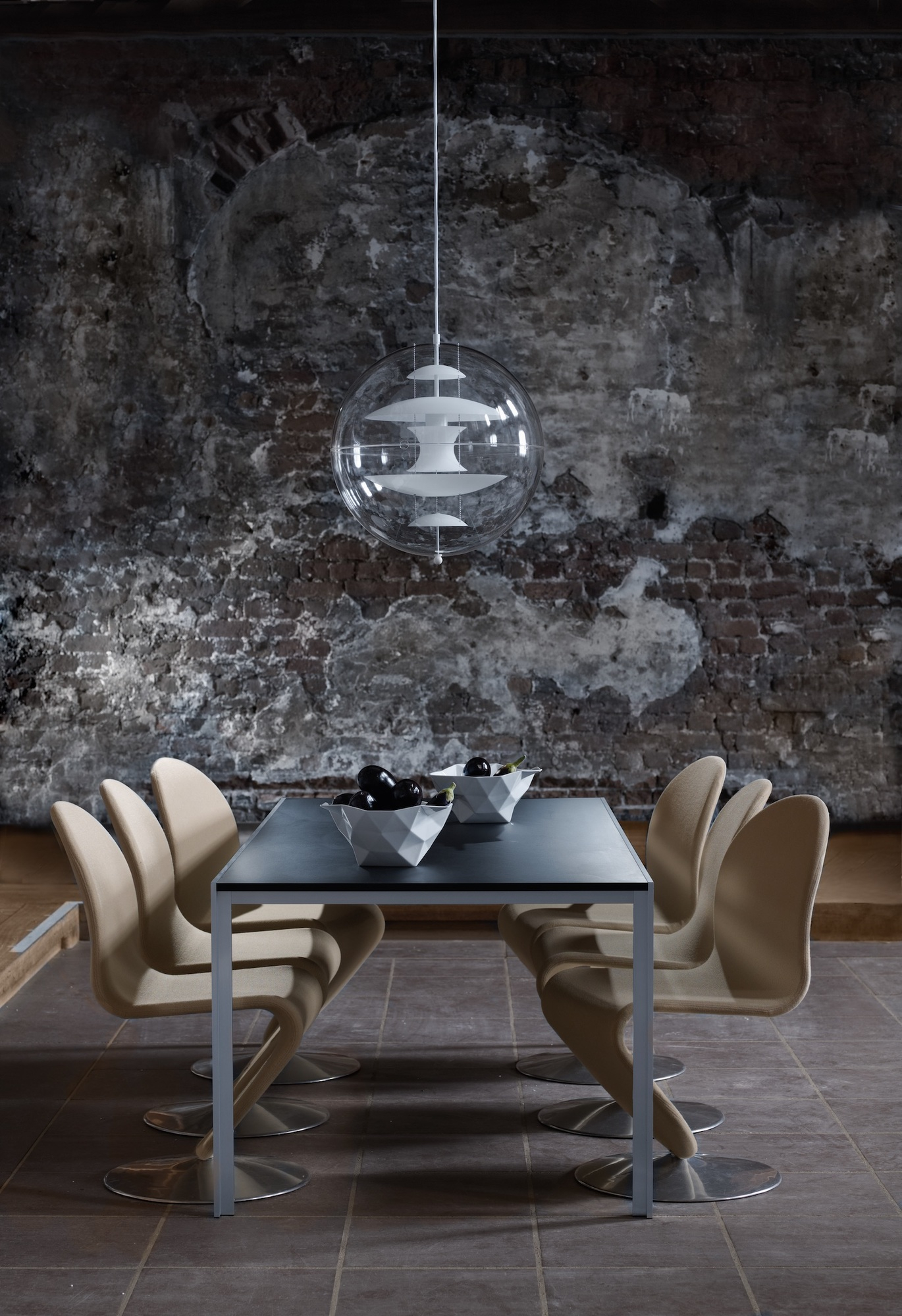 VP Globe Pendelleuchte von Verpan über Esstisch mit Stühlen vor einer Backsteinwand.
