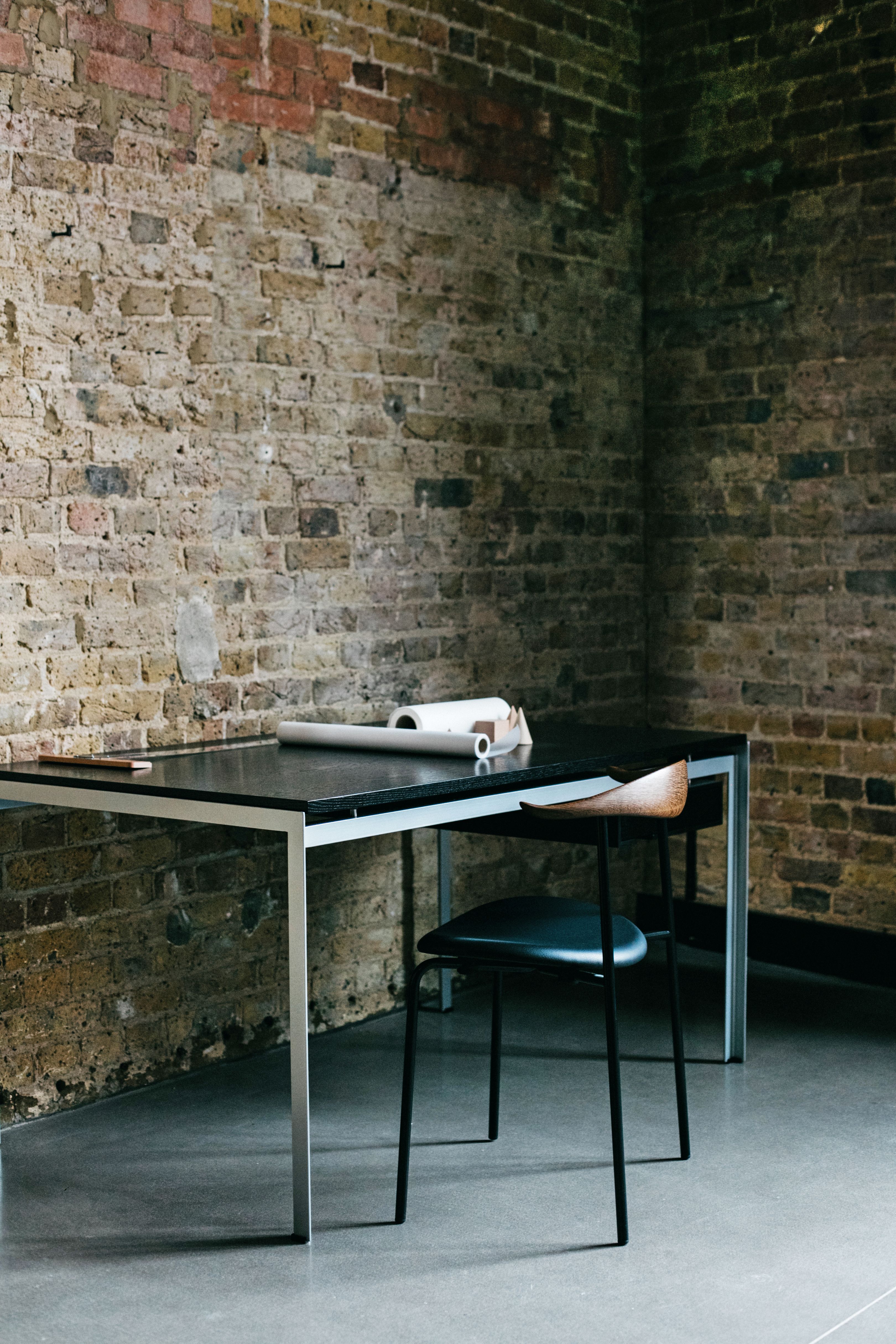 Carl Hansen & Søn PK52A Schreibtisch mit Stuhl vor einer Backsteinwand. Moderner Schreibtisch für Studenten.