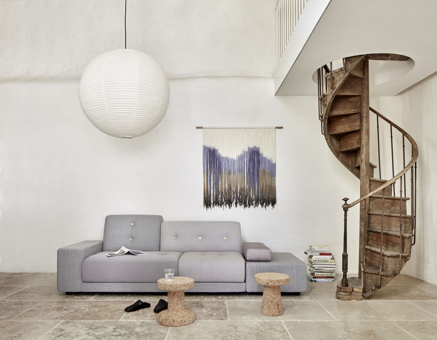 Graues Polder Sofa von Vitra in modernem Wohnzimmer mit Wendeltreppe und Korkhockern.
