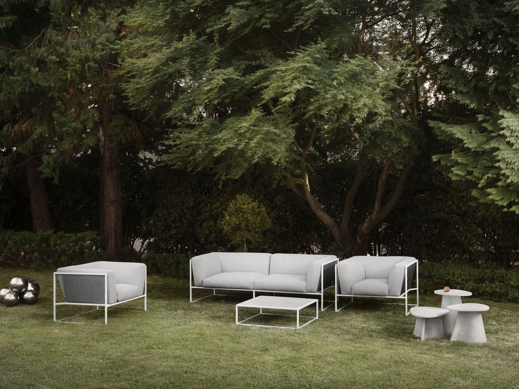 Graue Outdoor-Lounge-Möbel: Sofa, Sessel, Couchtisch und Beistelltische auf Rasen vor Bäumen. Gartenmöbel-Set für Terrasse.