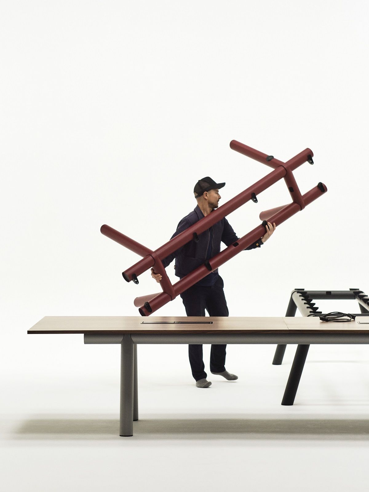 Mann montiert Hay Boa Table Konferenztisch mit braunem Gestell und Holzplatte.