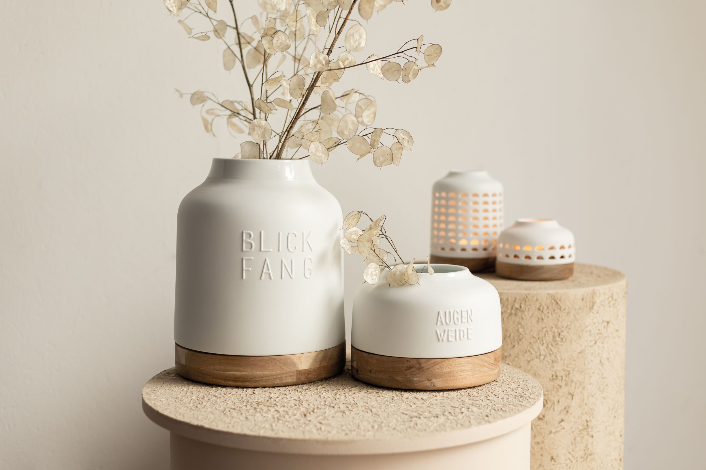 Weiße Räder Vase "Blickfang" mit Holzfuß und Trockenblumen, dekorative Wohnaccessoires im Hintergrund.