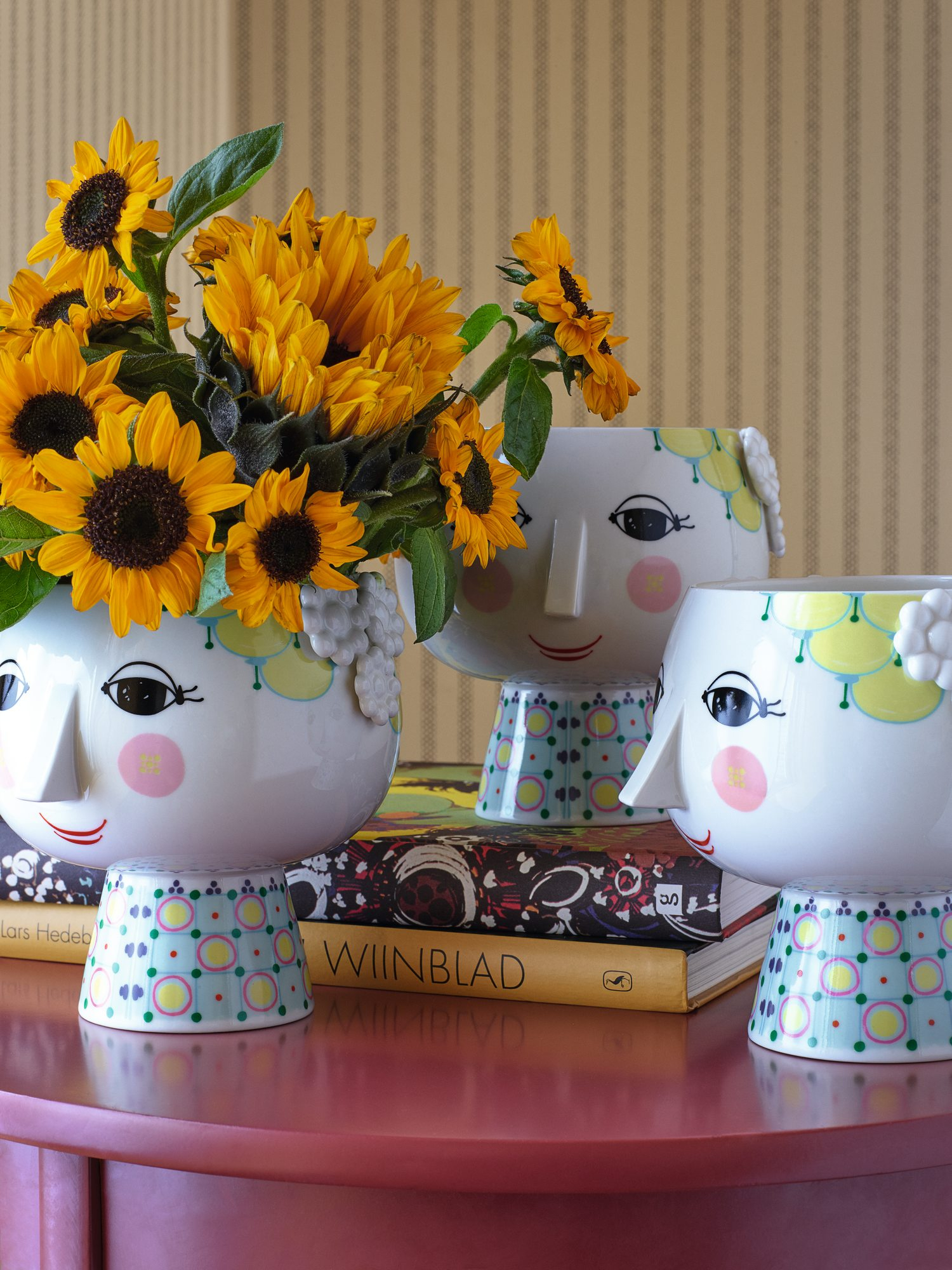Drei Bjorn Wiinblad Übertöpfe "Eva" mit Gesicht und Sonnenblumen auf einem Tisch.