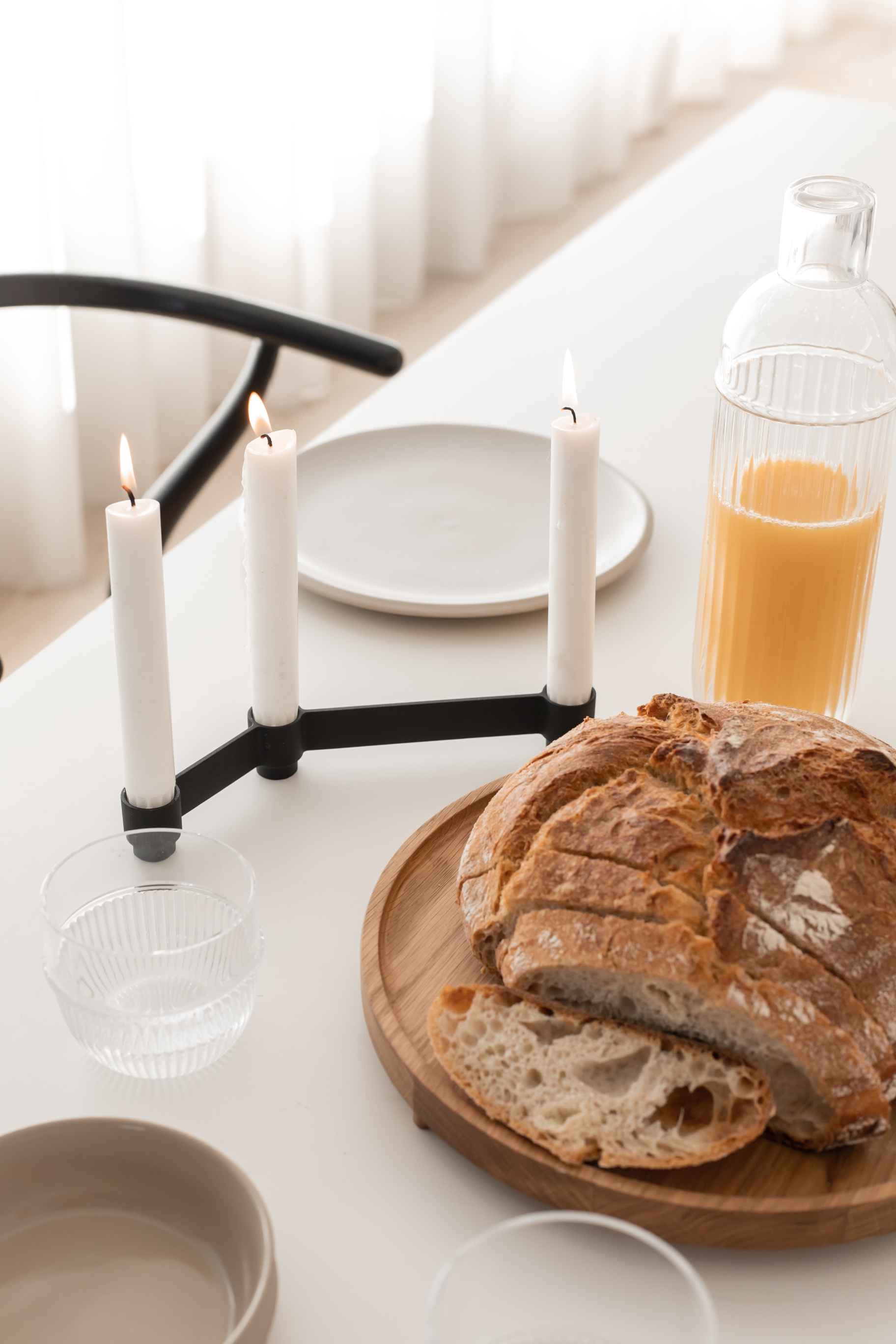 Sero Kerzenständer mit drei brennenden Kerzen, Brot, Saft und Geschirr auf weißem Tisch.
