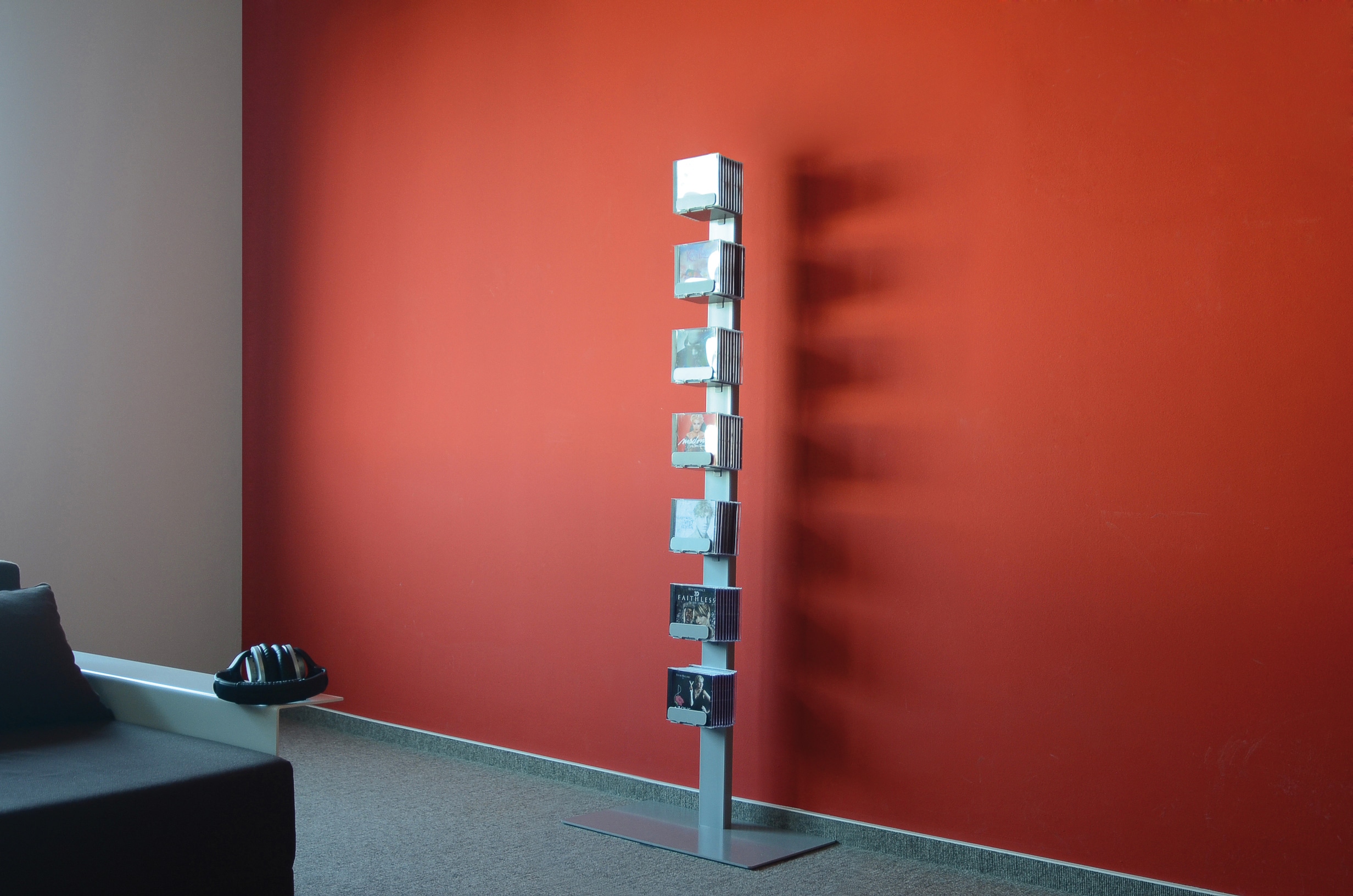 Silbernes CD-Regal "CD-Baum" mit CDs vor roter Wand. Einzeln stehendes Standregal für Musiksammlungen.