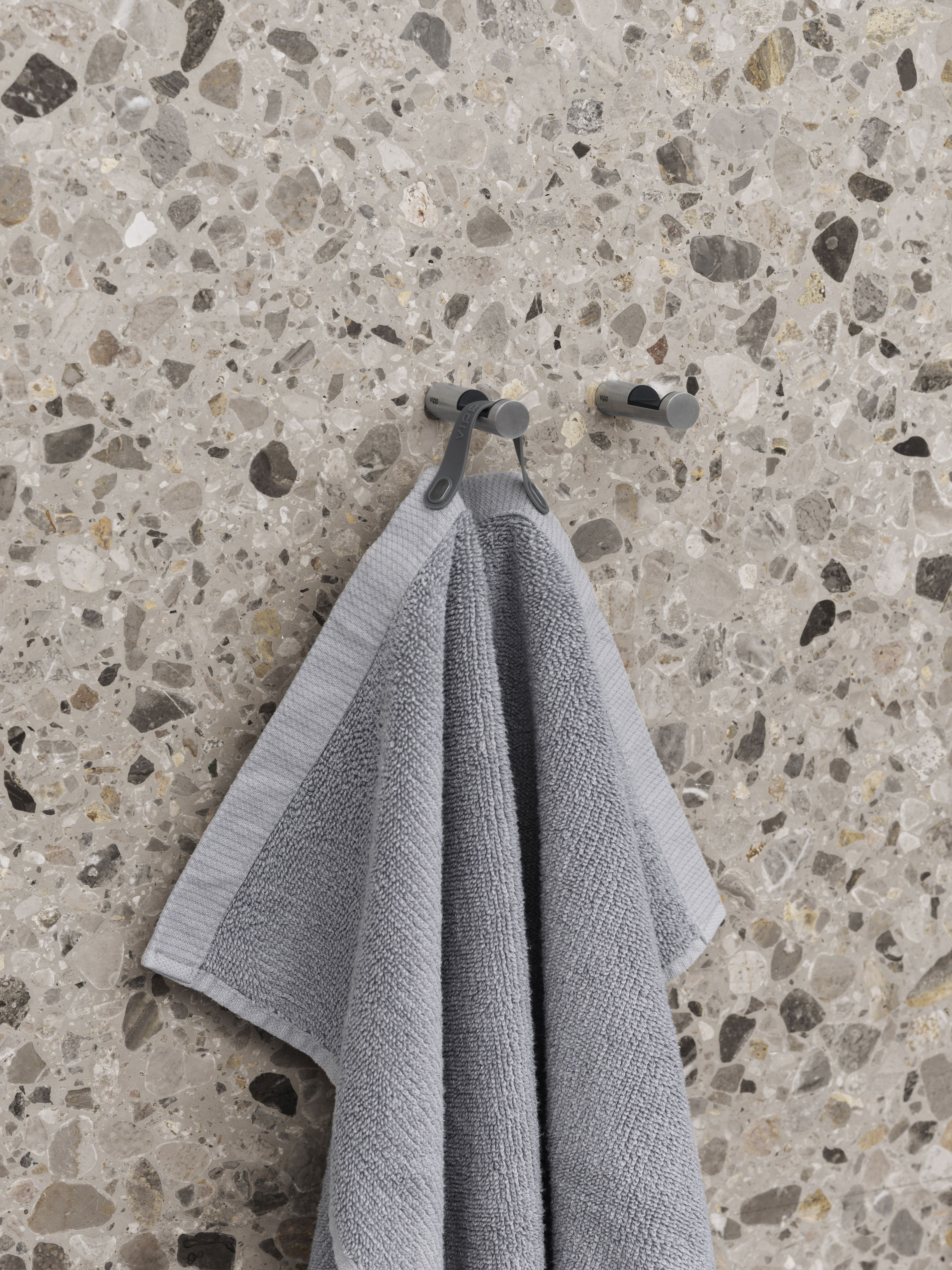 Graues Handtuch hängt an Vipp Handtuchhaken (2er-Set) vor einer gemusterten Wand.