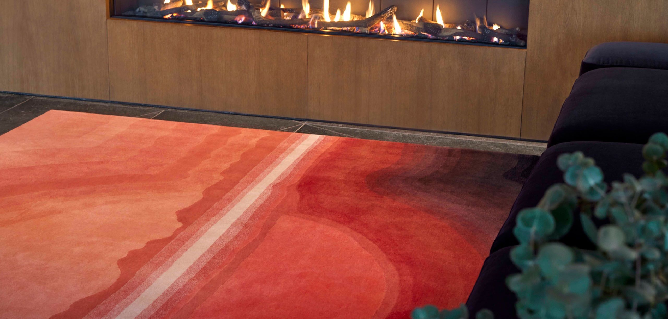 Sunset Rug Teppich mit Farbverlauf in Rot- und Orangetönen vor einem Kamin.