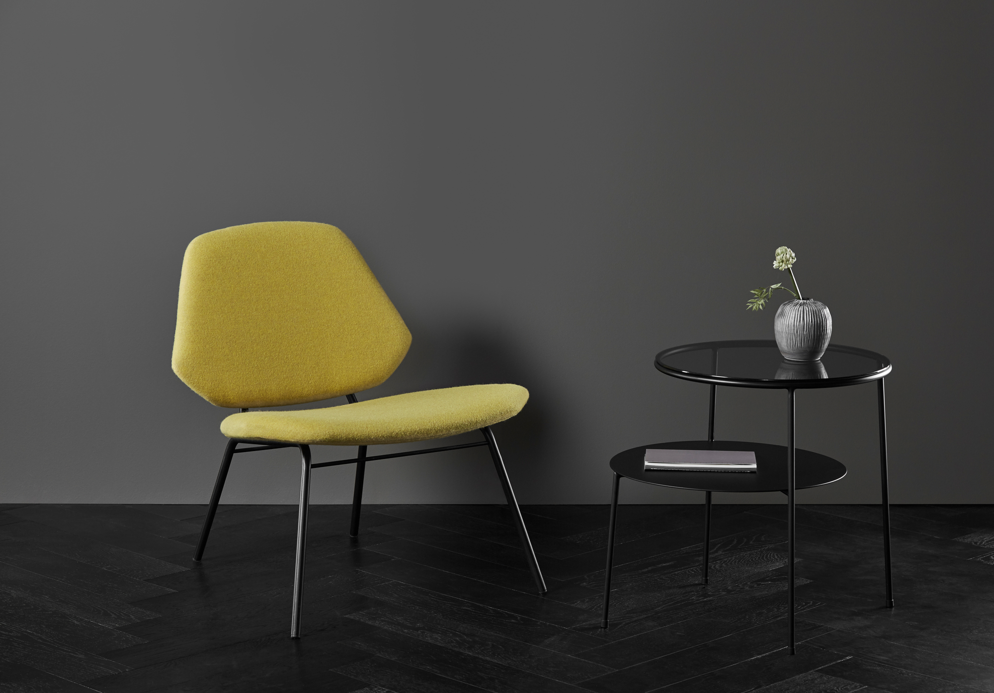 Duo Beistelltisch von Woud, schwarz mit dunklem Rauchglas, neben einem gelben Stuhl.