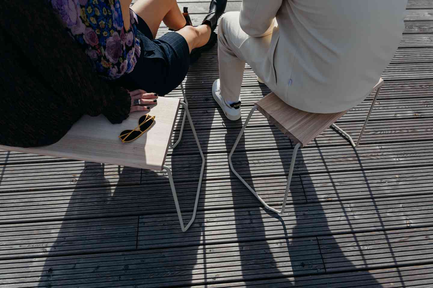 Zwei Personen sitzen auf D:003 Beistellhockern. Holz-Hocker mit Metallgestell, ideal als Sitzmöbel und Beistelltisch.