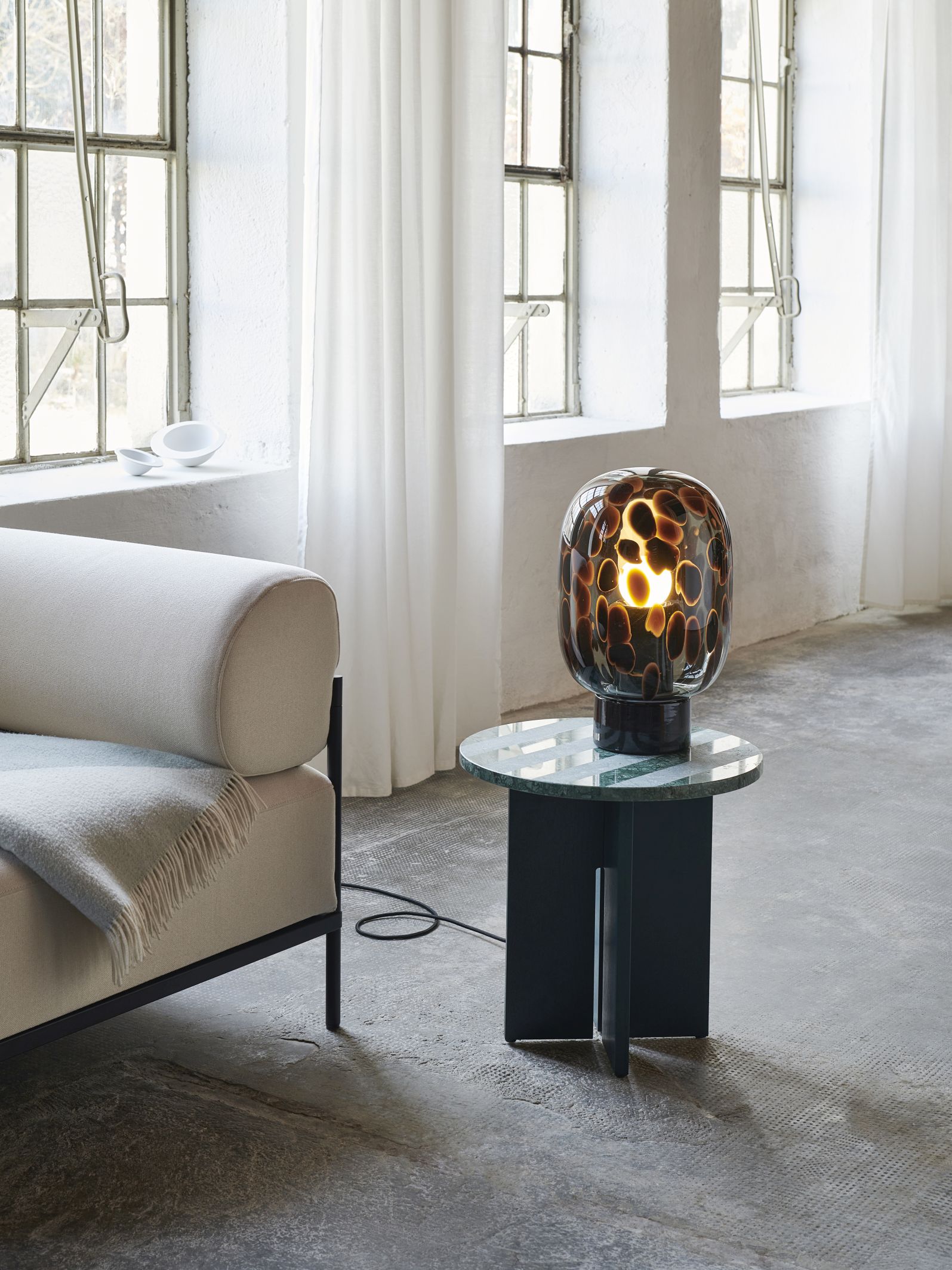 Flakes Tischleuchte Favius in Rauchgrau und Schwarz auf einem Beistelltisch im Interieur.