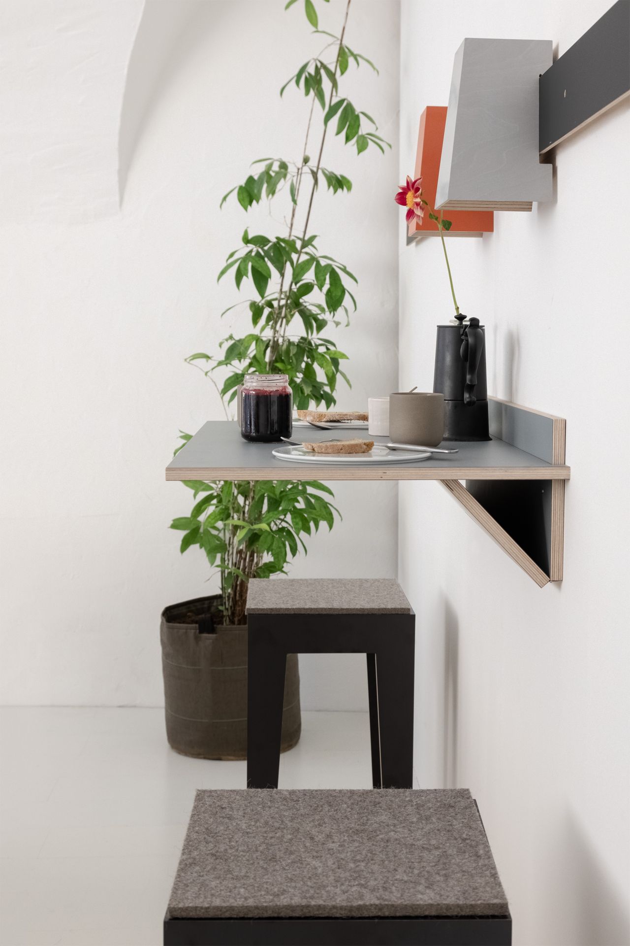Wandklapptisch mit Frühstück, Stuhl und Pflanze. Modernes platzsparendes Möbeldesign für kleine Räume.
