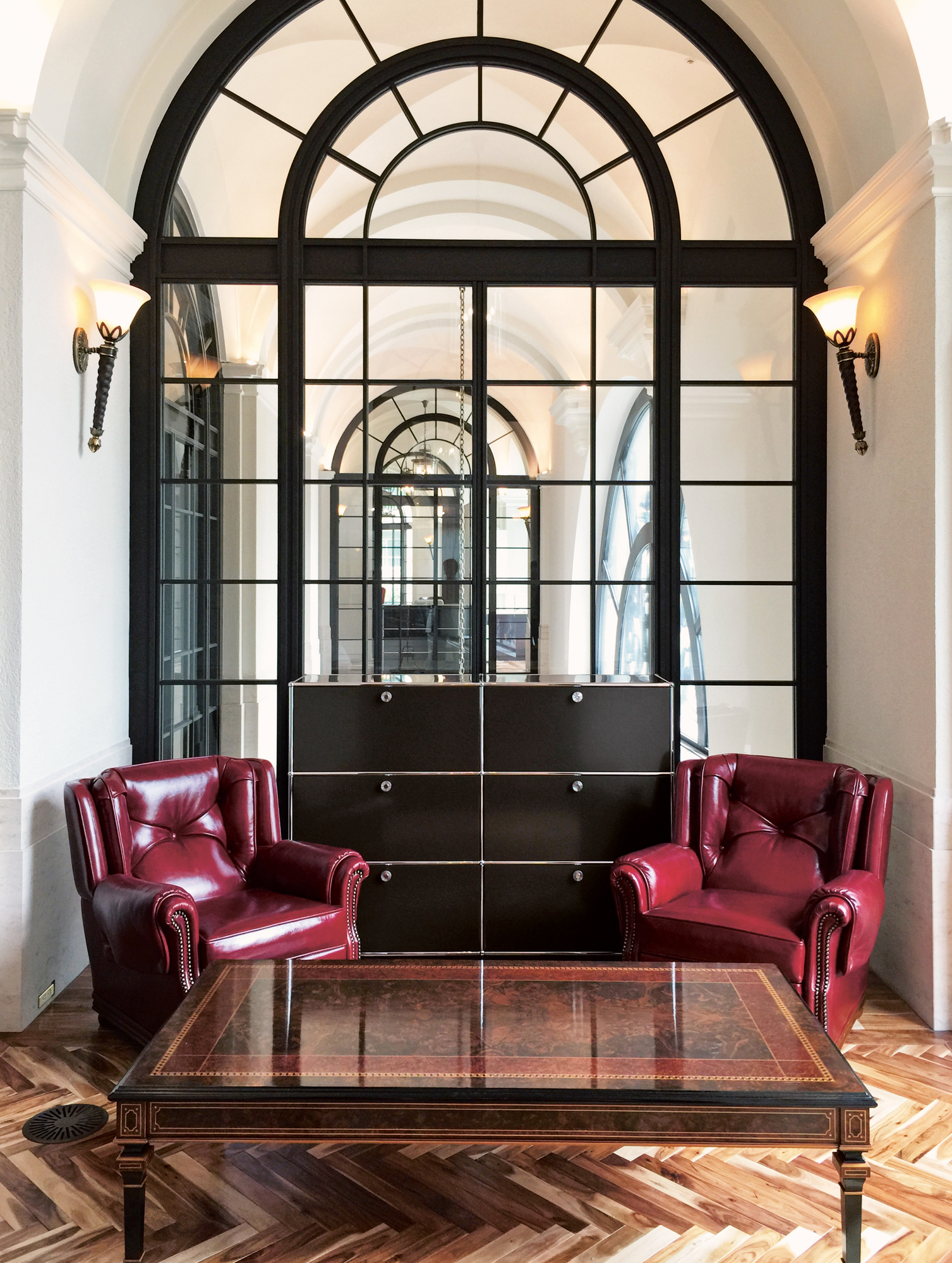 USM Haller Highboard mit sechs Klappen in Schwarz, kombiniert mit roten Ledersesseln und Holztisch.