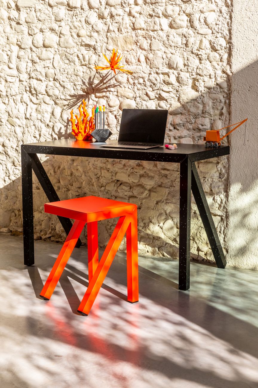 Bureaurama Hocker von Magis, orangefarbener Barhocker vor Schreibtisch und Steinwand. Design Büromöbel.