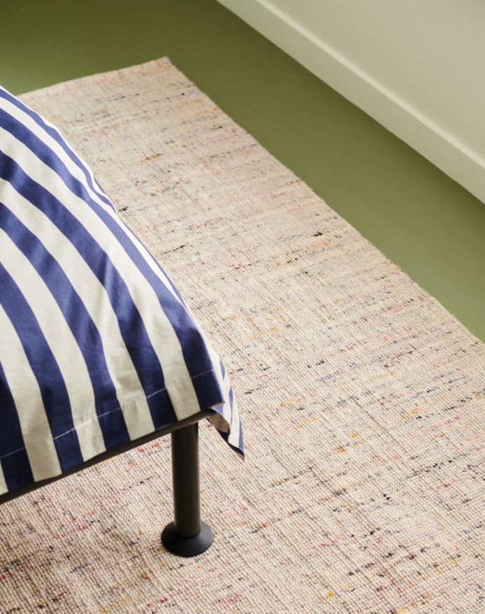 Beiger Crayon Rug Teppich von Hay unter einem Bett mit blau-weiß gestreifter Bettwäsche.