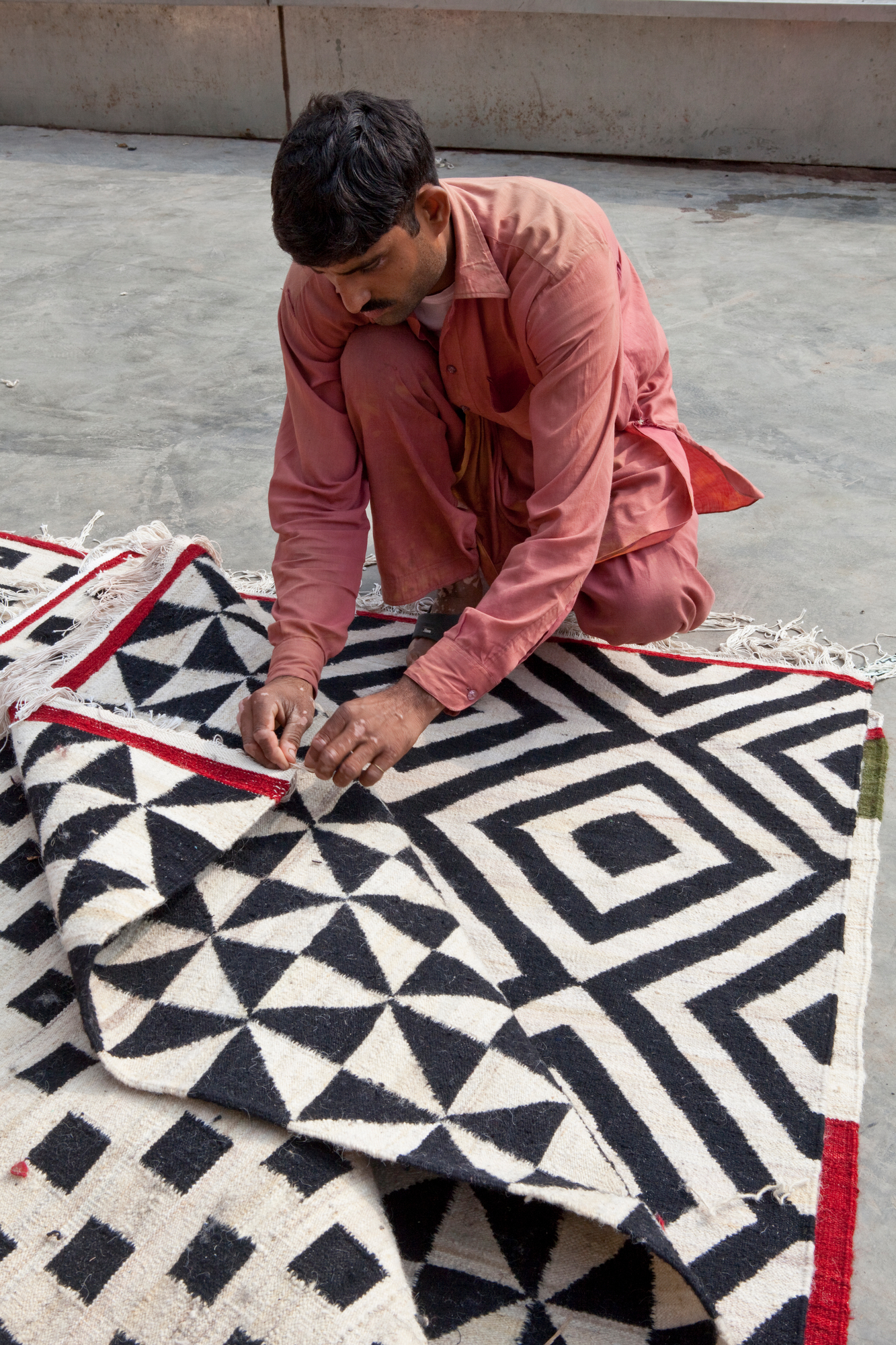 Mann inspiziert Nanimarquina Teppich mit geometrischem Muster, handgefertigter Wollteppich für Wohnzimmer.