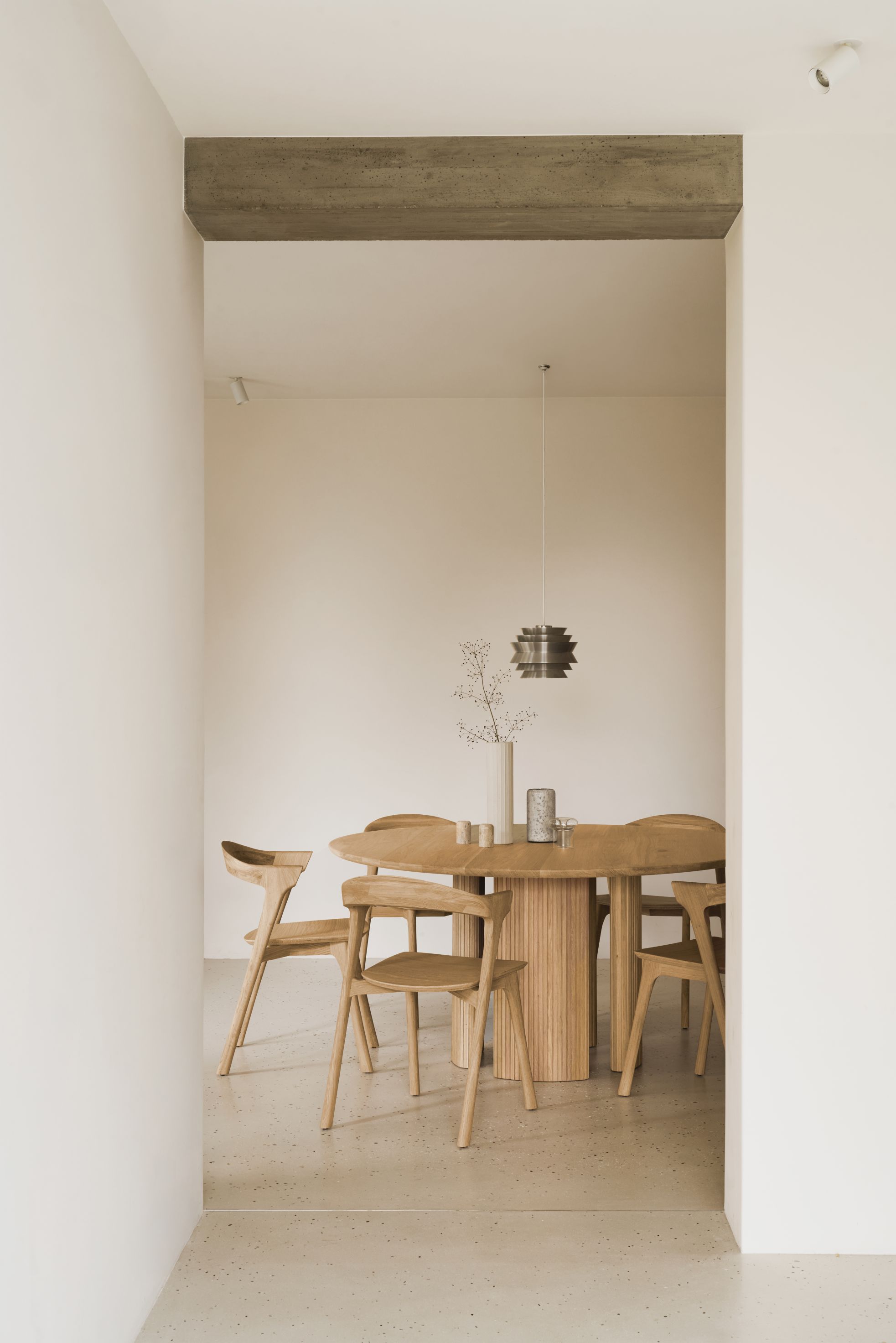 Ethnicraft Roller Max Tisch: Runder Holztisch mit geriffeltem Sockel und passenden Holzstühlen in minimalistischem Interieur.