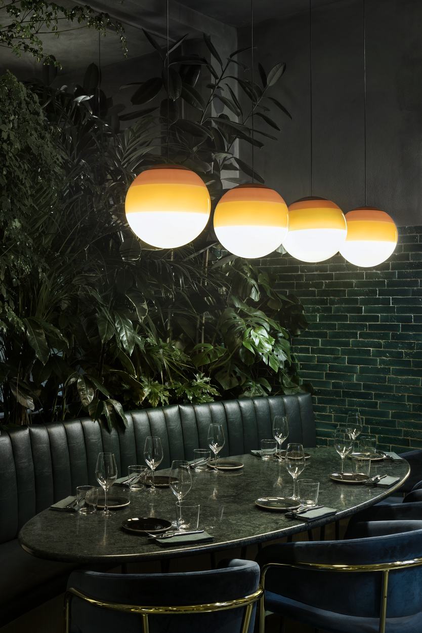 Reihe von Dipping Light Pendelleuchten in Bernstein über gedecktem Tisch, stimmungsvolle Beleuchtung.