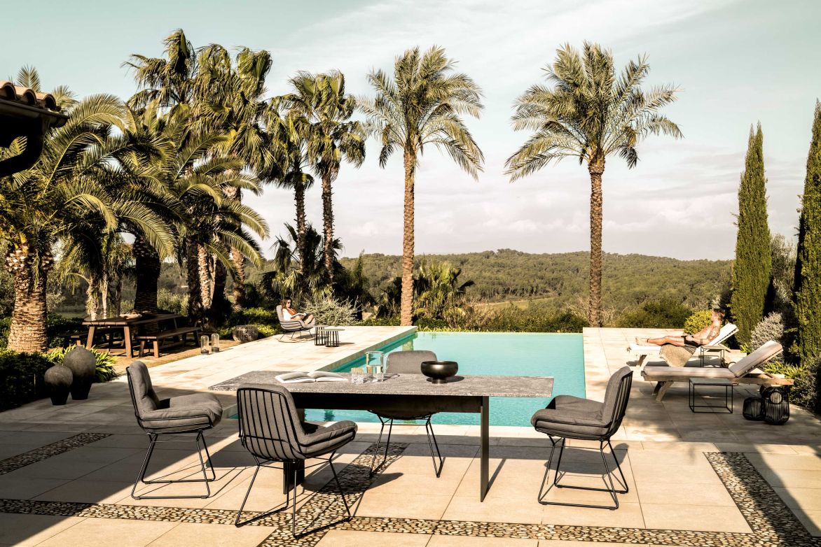 SC 41 Outdoor Tisch Stein Alps Glitter Janua am Pool, mit Stühlen und mediterraner Landschaft.