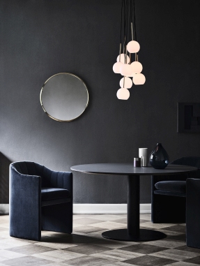 Blauer Loafer Sessel von AndTradition neben einem runden Esstisch in dunklem Interieur.