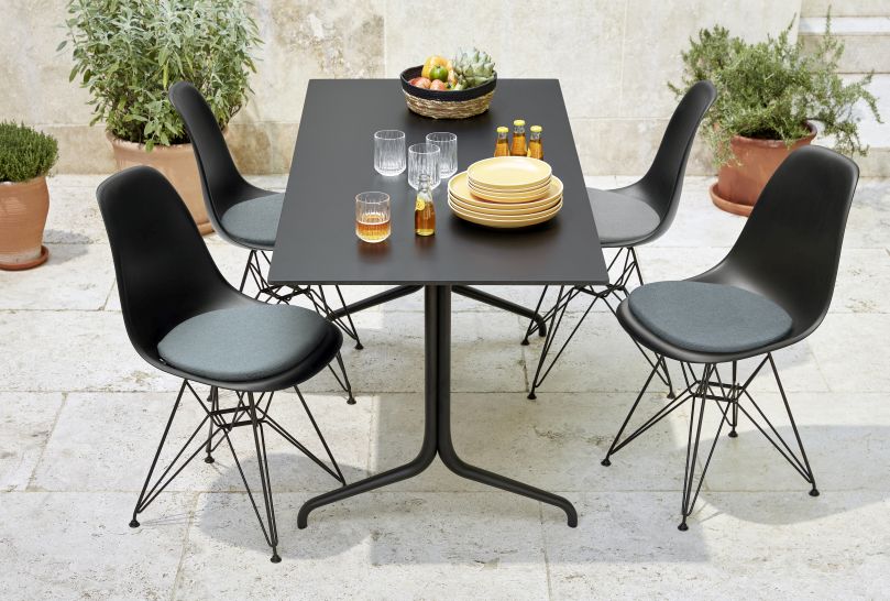 Schwarze Stühle mit Soft Seats Sitzkissen von Vitra um einen dunklen Tisch im Außenbereich.