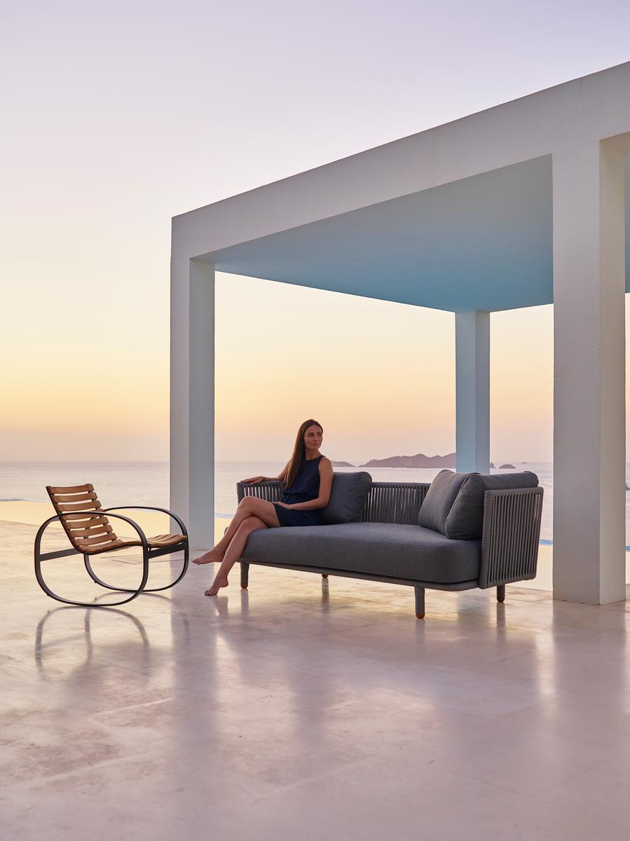 Frau entspannt auf Cane-Line Moments Outdoor Sofa mit Meerblick. Gartenmöbel für stilvolle Entspannung.