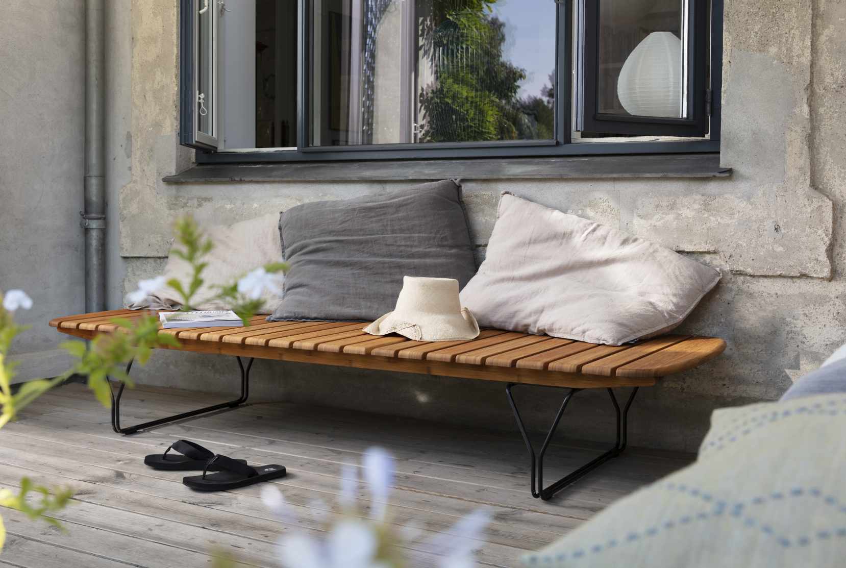 Molo Sonnenliege von Houe: Outdoor-Holzliege mit Kissen und Hut auf einer Terrasse.