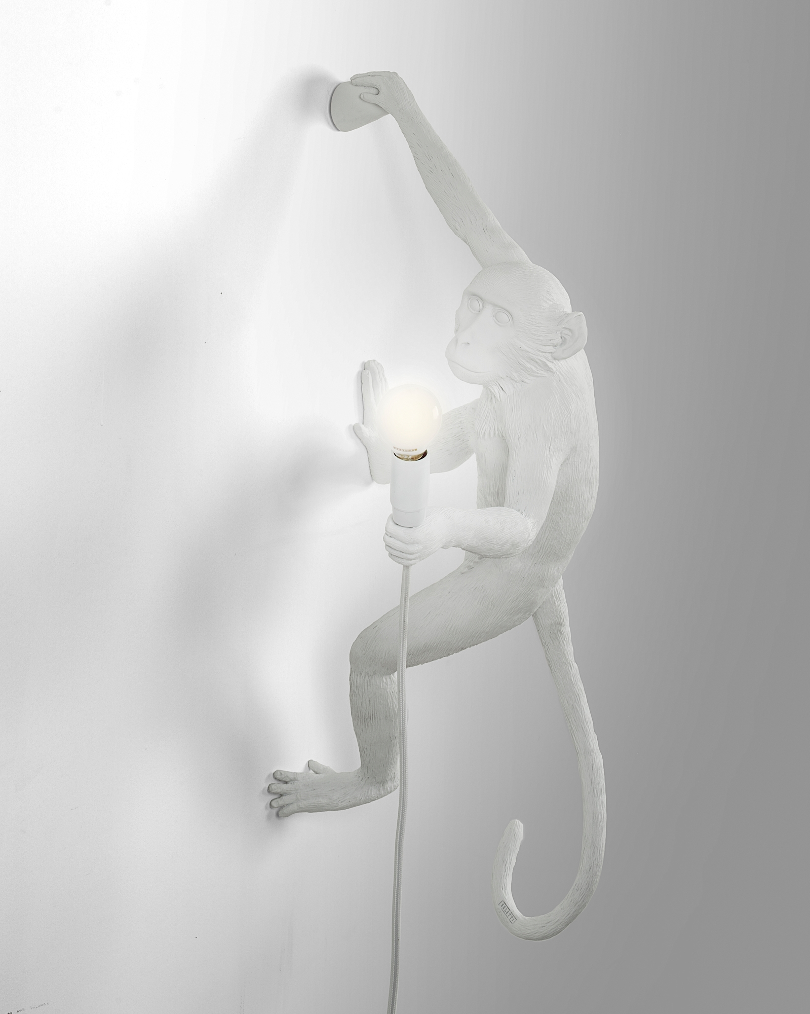 Weiße Seletti Monkey Lamp Wandleuchte rechts, ein Affe hält eine Glühbirne an der Wand.