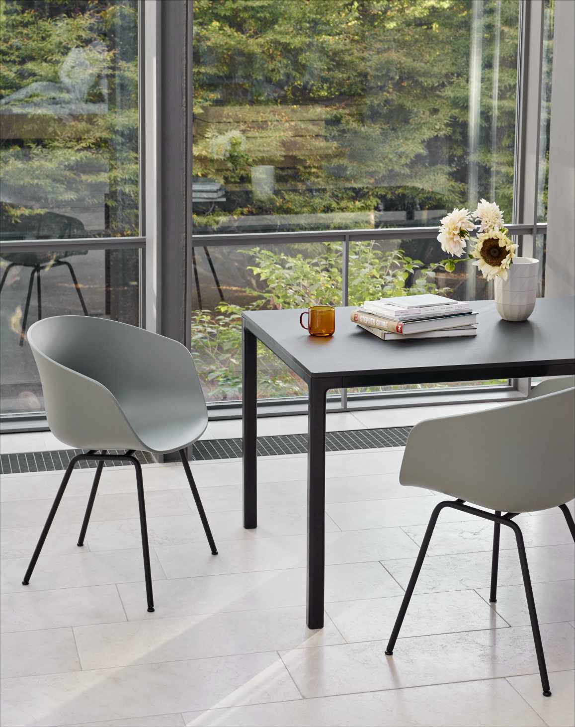 Heller Raum mit zwei grauen About A Chair AAC 26 Stühlen und schwarzem Tisch.