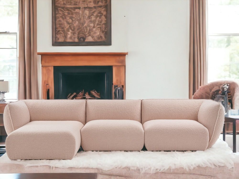 Beiges Mia Modulsofa von Freifrau Manufaktur mit Bouclé-Bezug vor Kamin und Kunstwerk.