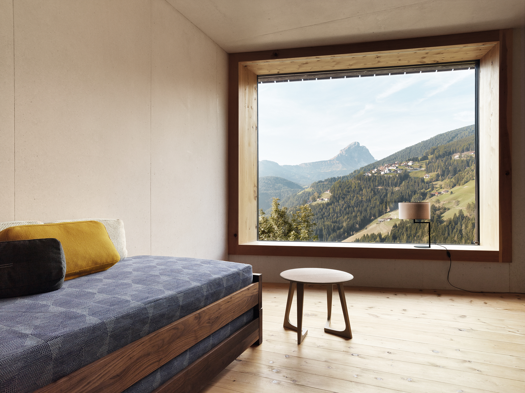 Guest 90 Holzbett aus Nussbaum mit blauem Bezug und Blick auf die Berge.