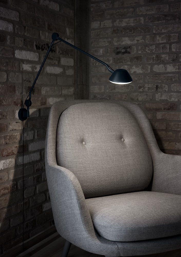 AQ01 Wandleuchte von Fritz Hansen, weiße Design Lampe über einem Sessel an Backsteinwand.
