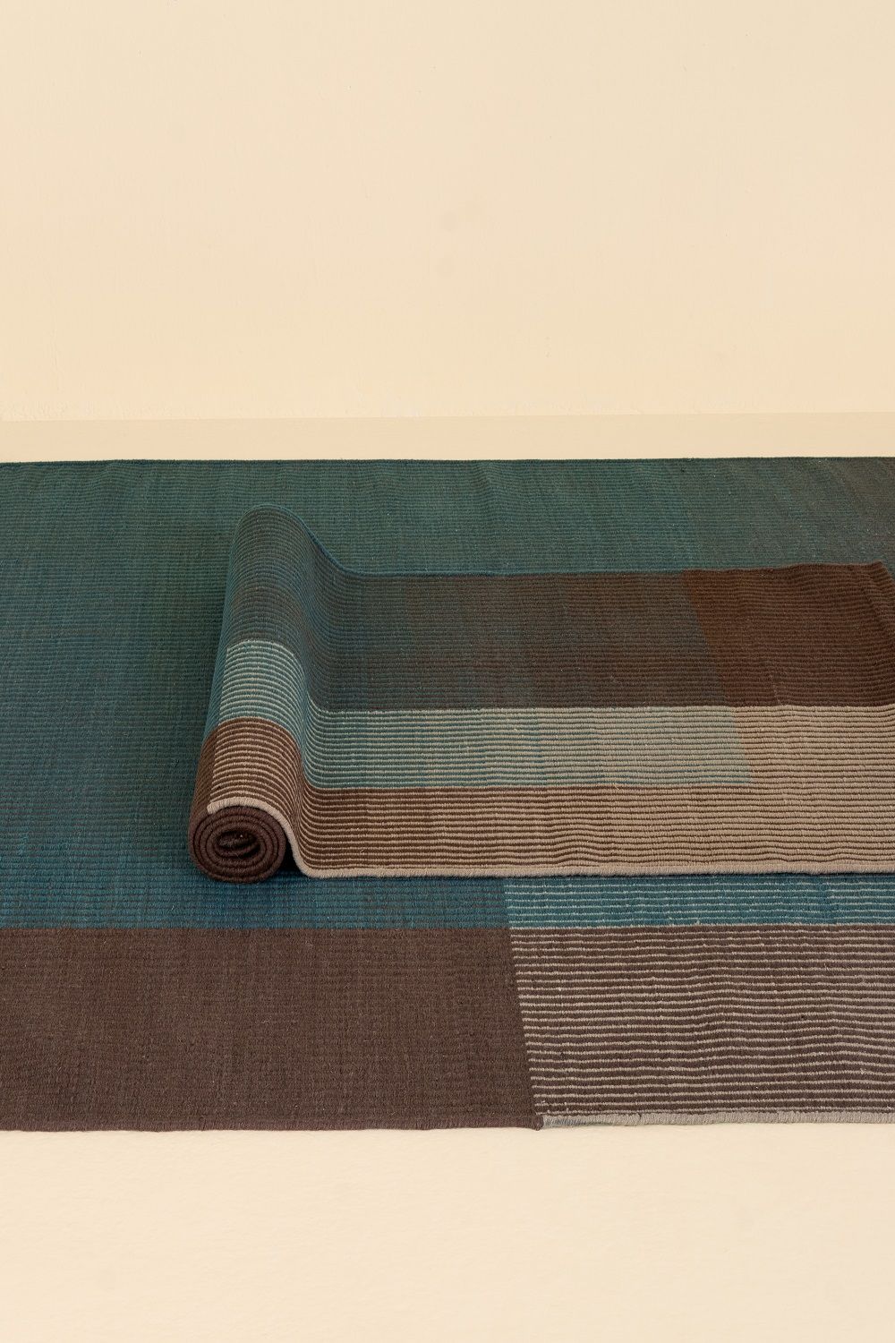 Detailaufnahme des Haze Runner Teppichs von Nanimarquina, teilweise aufgerollt, in Blau- und Brauntönen.