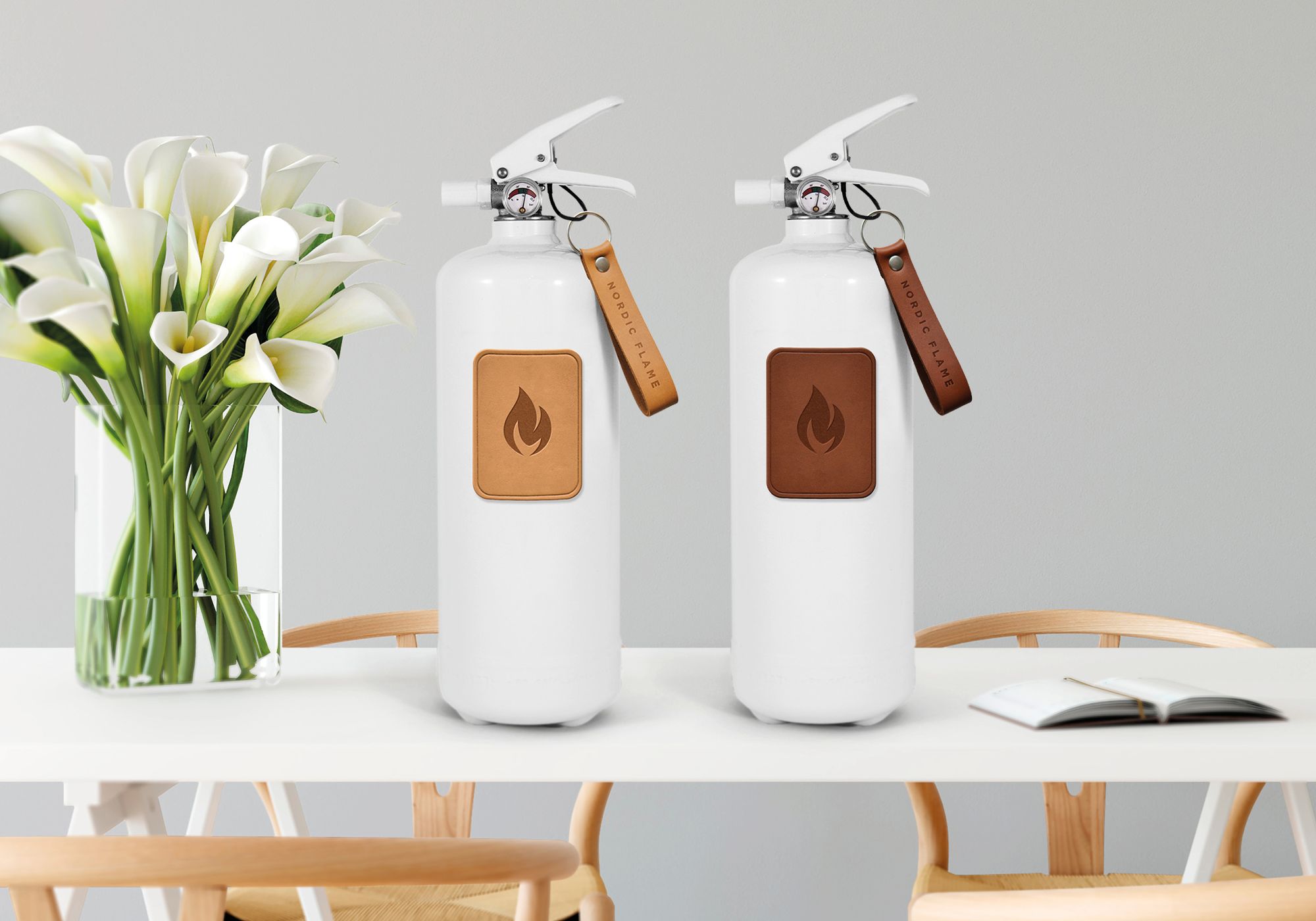 Zwei weiße Feuerlöscher mit Lederemblem von Nordic Flame auf einem Tisch.