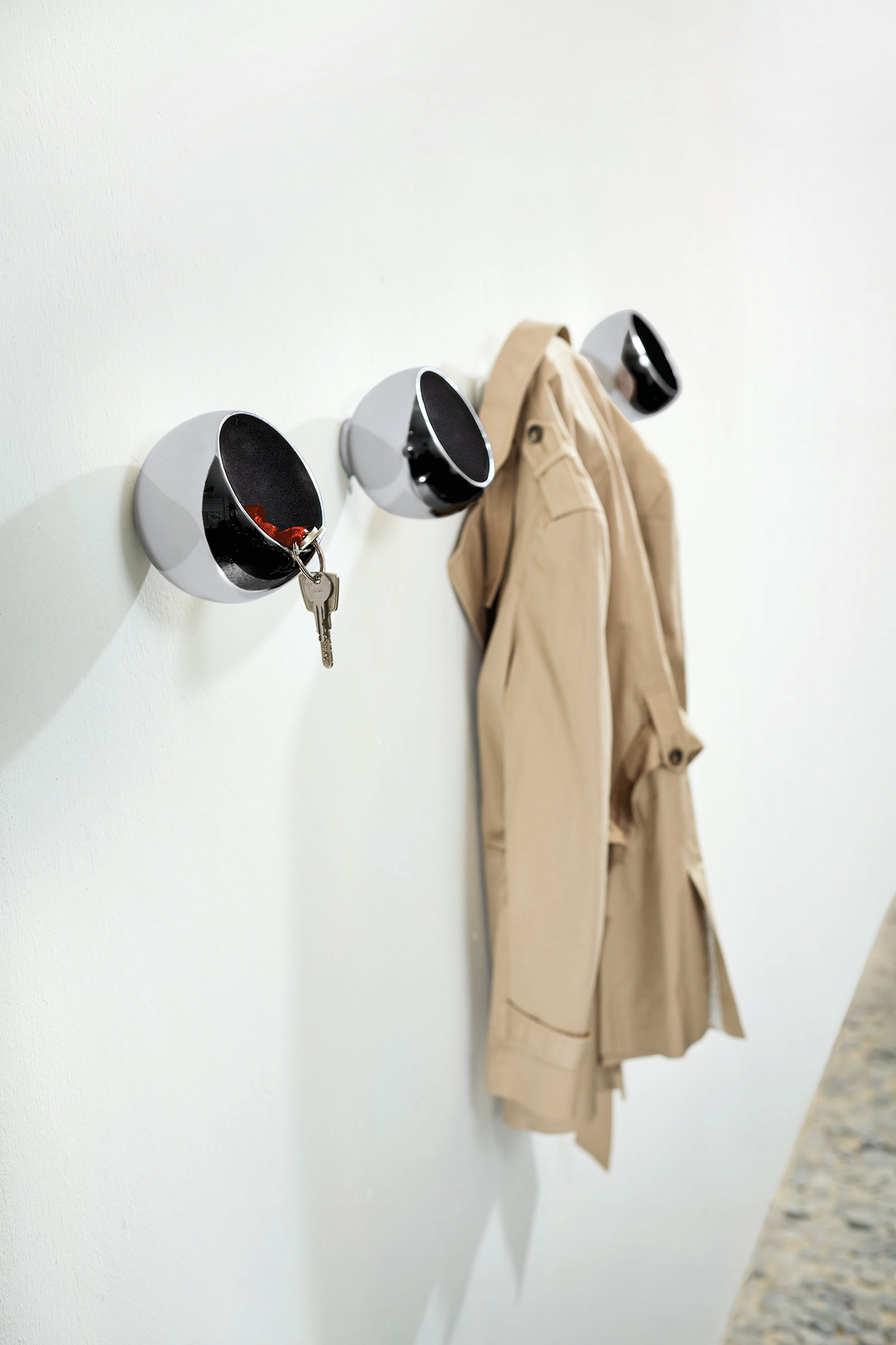 Drei Sphere Garderobenkugeln von Philippi an einer weißen Wand mit Mantel und Schlüssel.