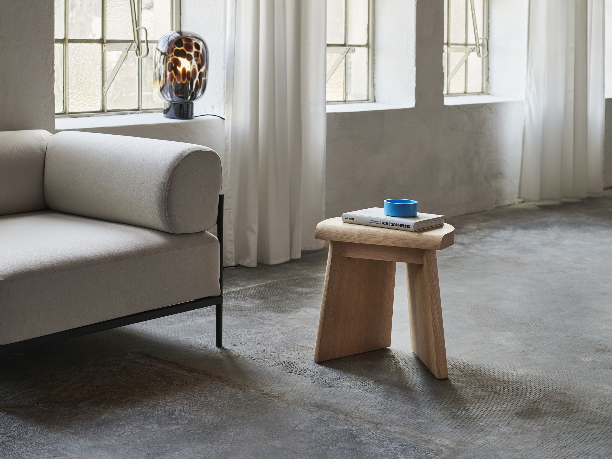 Flakes Tischleuchte Favius in Rauchgrau und Schwarz auf Fensterbank neben Sofa im Wohnzimmer.