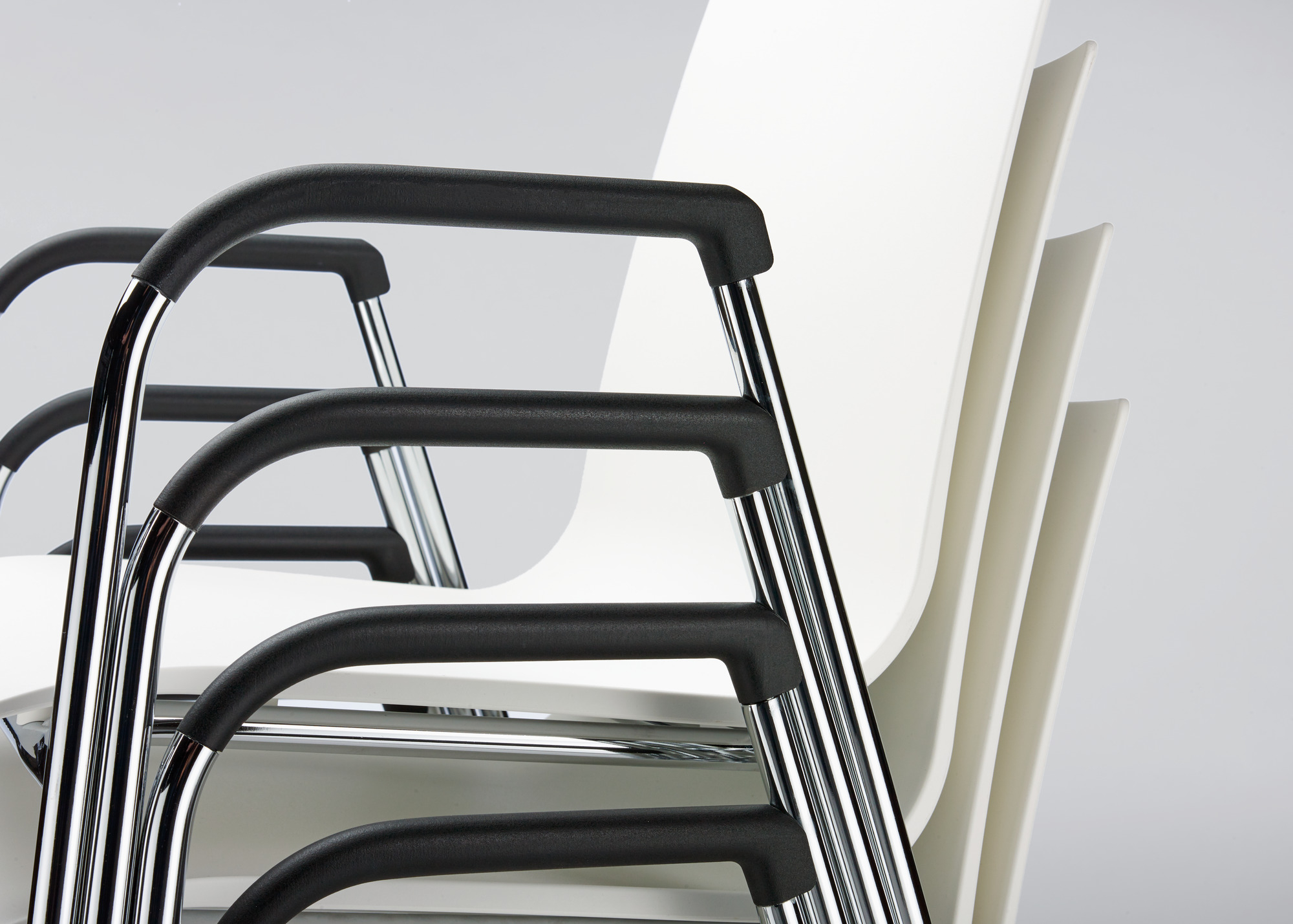 Detailaufnahme von gestapelten S 260 F Stühlen mit Armlehne von Thonet, weißer Sitzschale und Chromgestell.