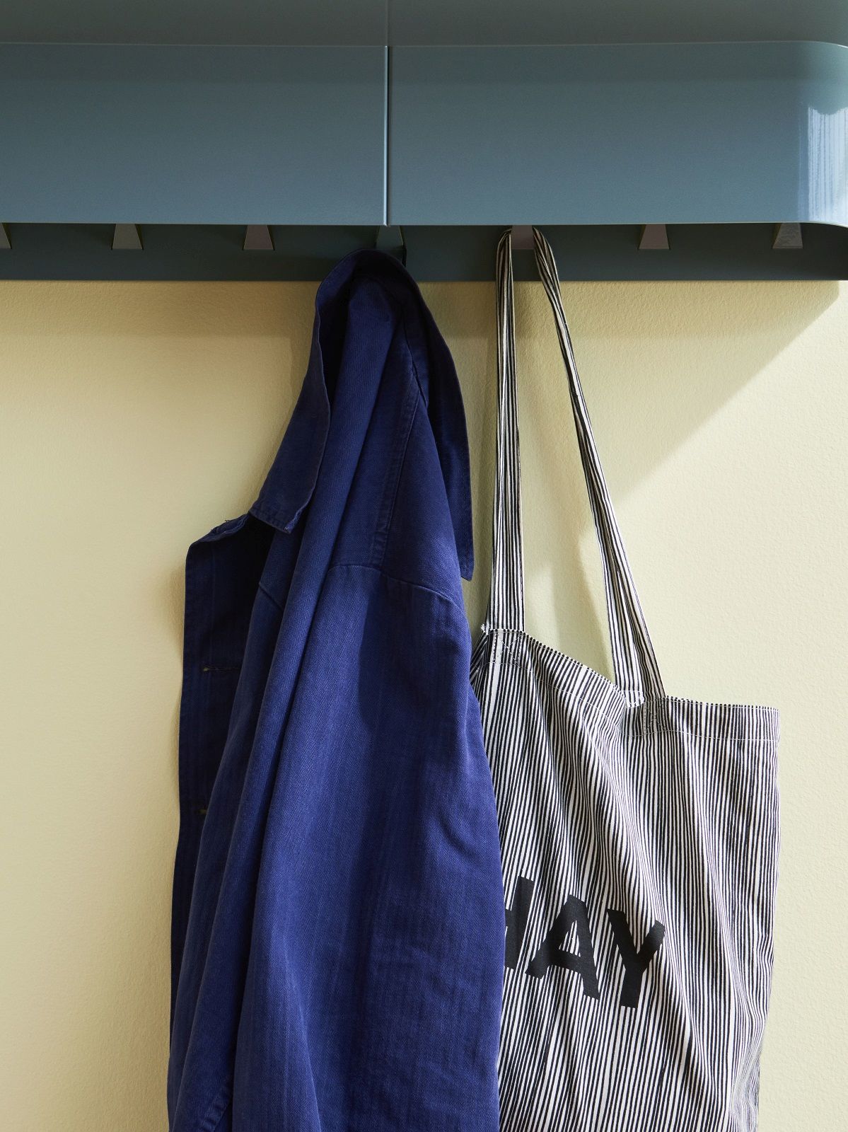 Blaues Hay Korpus Shelf Wandregal mit vier Haken, daran hängen Jacke und Tasche.